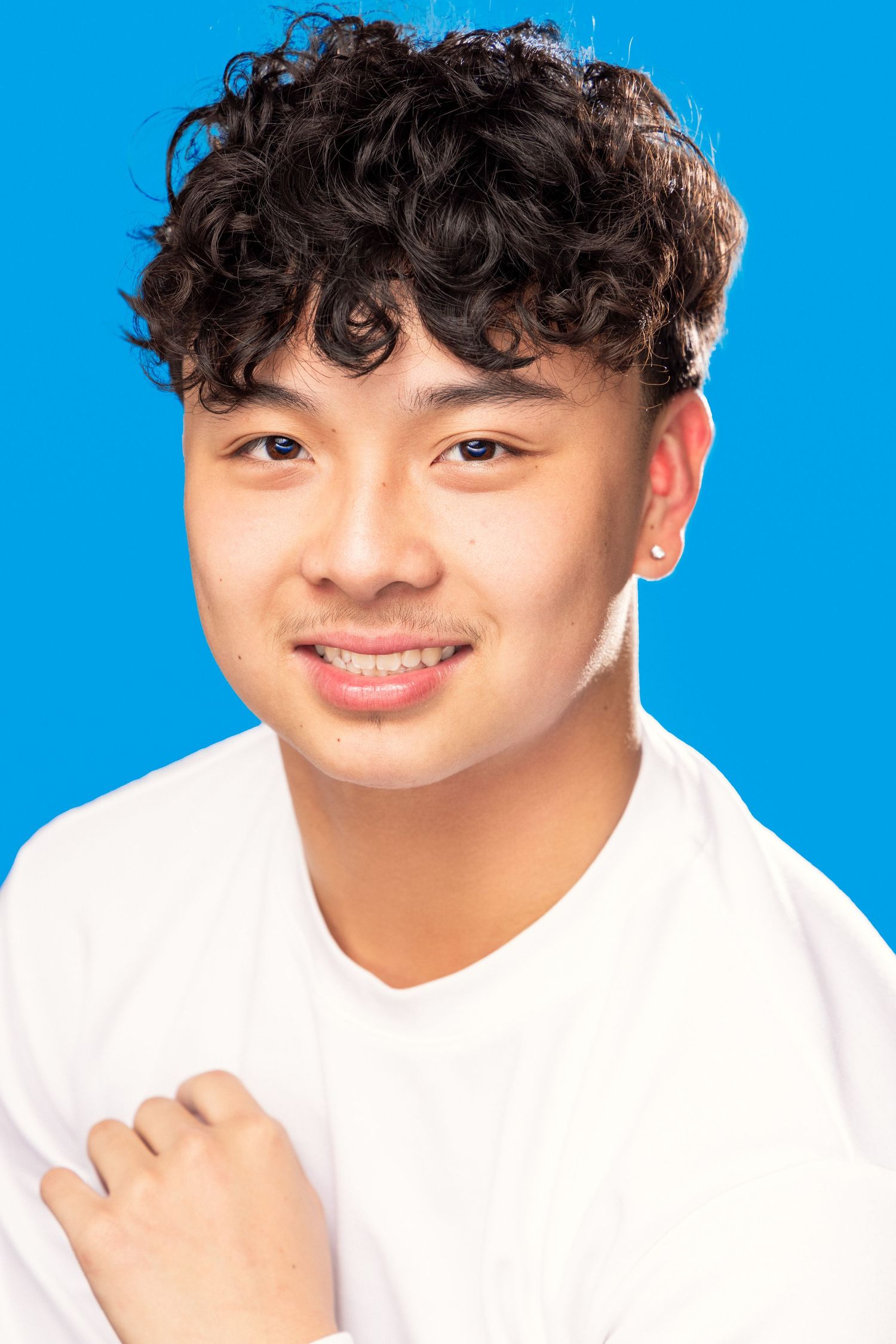 Person in white shirt against bright blue background makes playful expressions in headshot photo series.