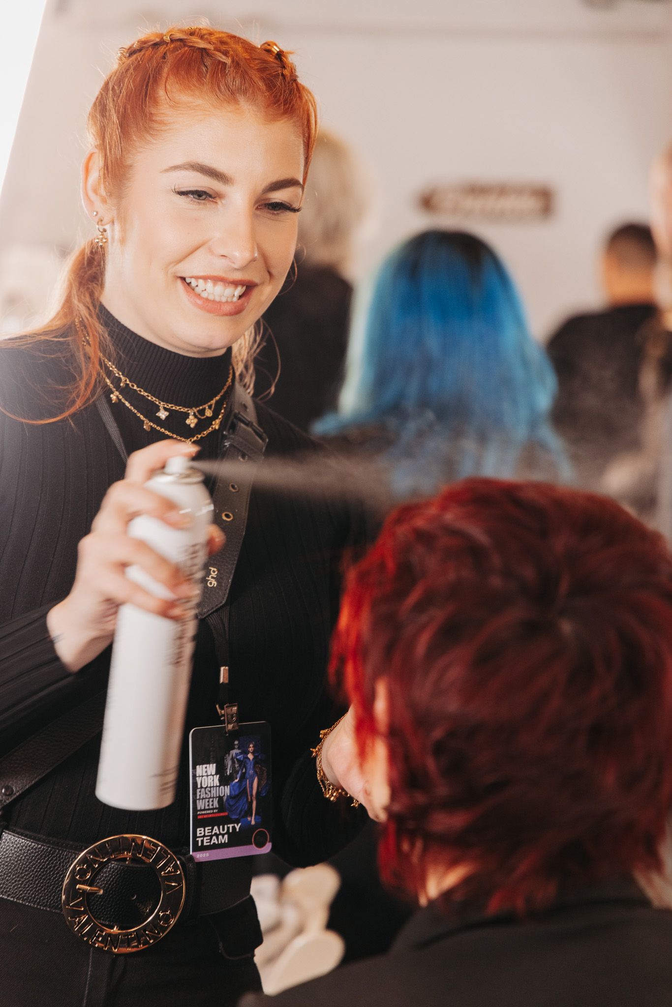 Makeup artist applies product backstage at fashion event wearing black turtleneck.