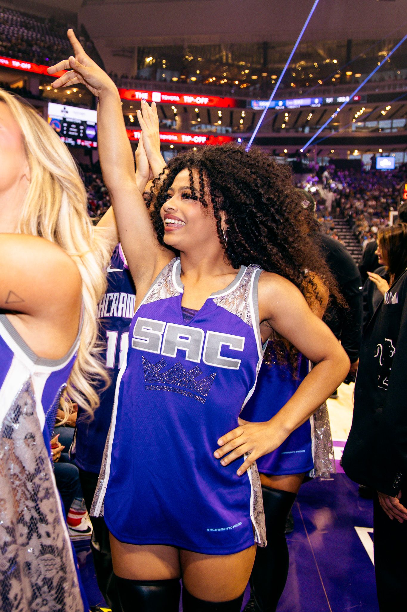 Sacramento Kings cheerleader in purple SAC jersey performs at NBA game inside Golden 1 Center arena.