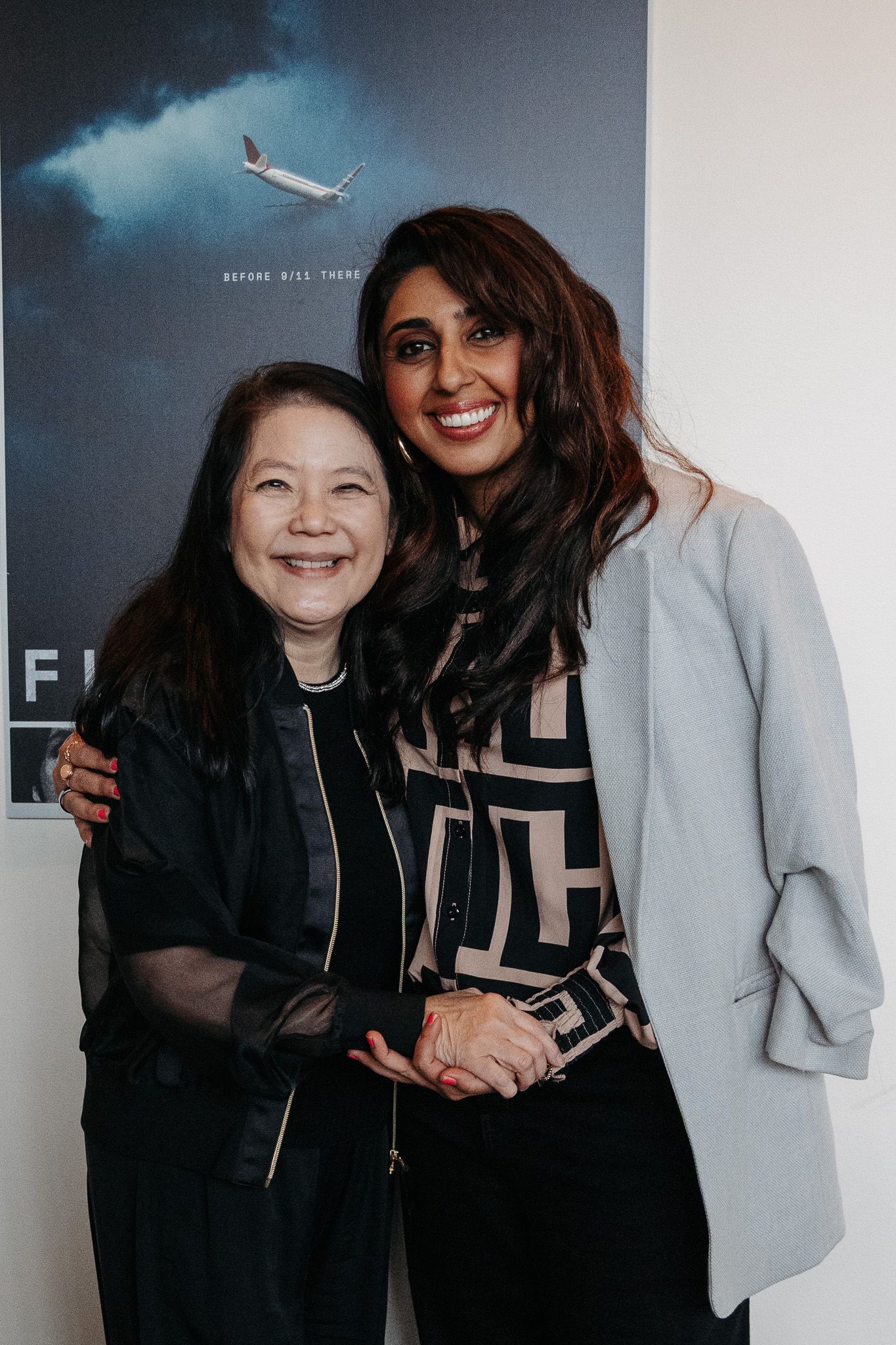 Two women pose together at an event with an airplane movie poster in the background.
