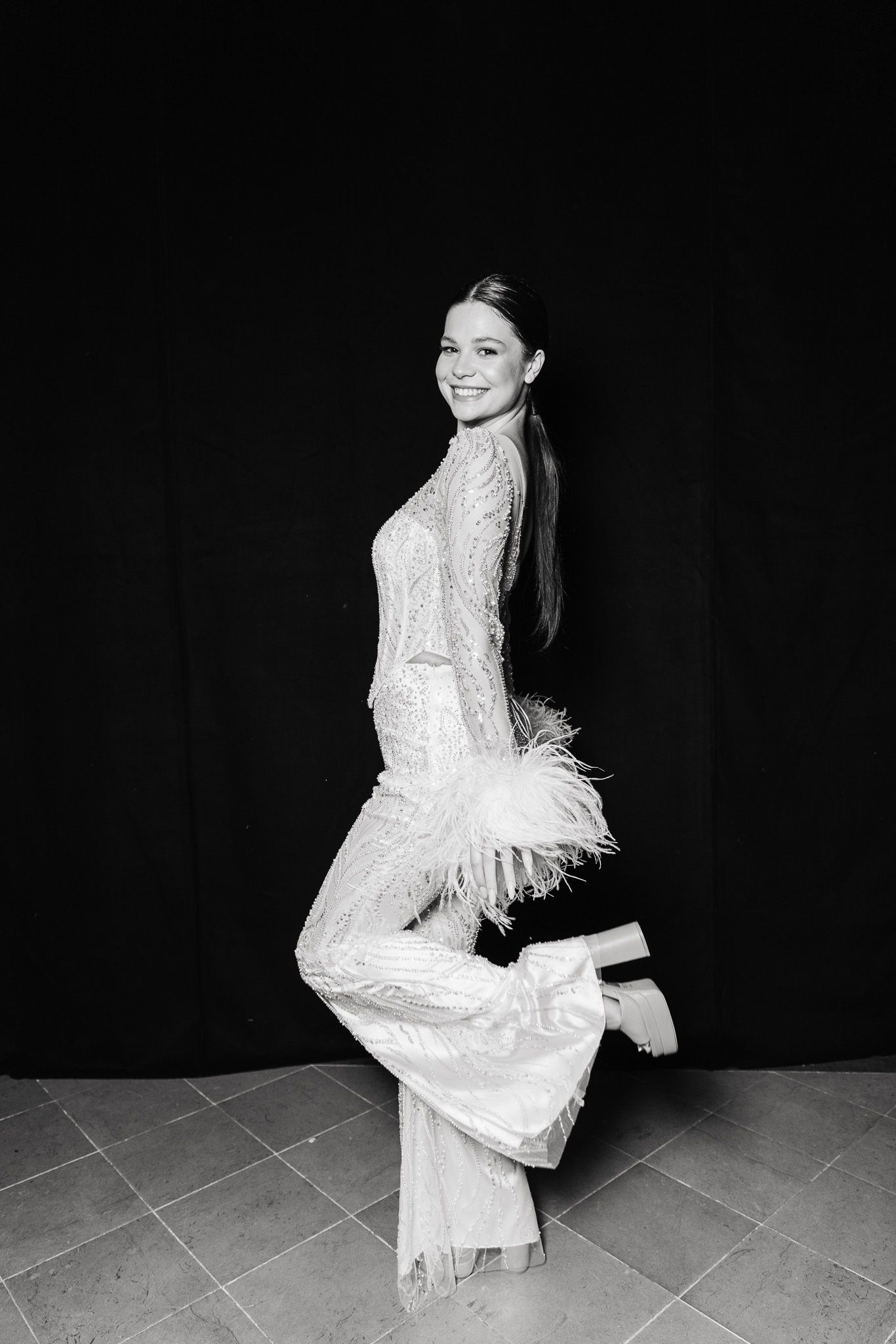 A figure in a white lace dress with feather details poses against a black background in a series of artistic shots.