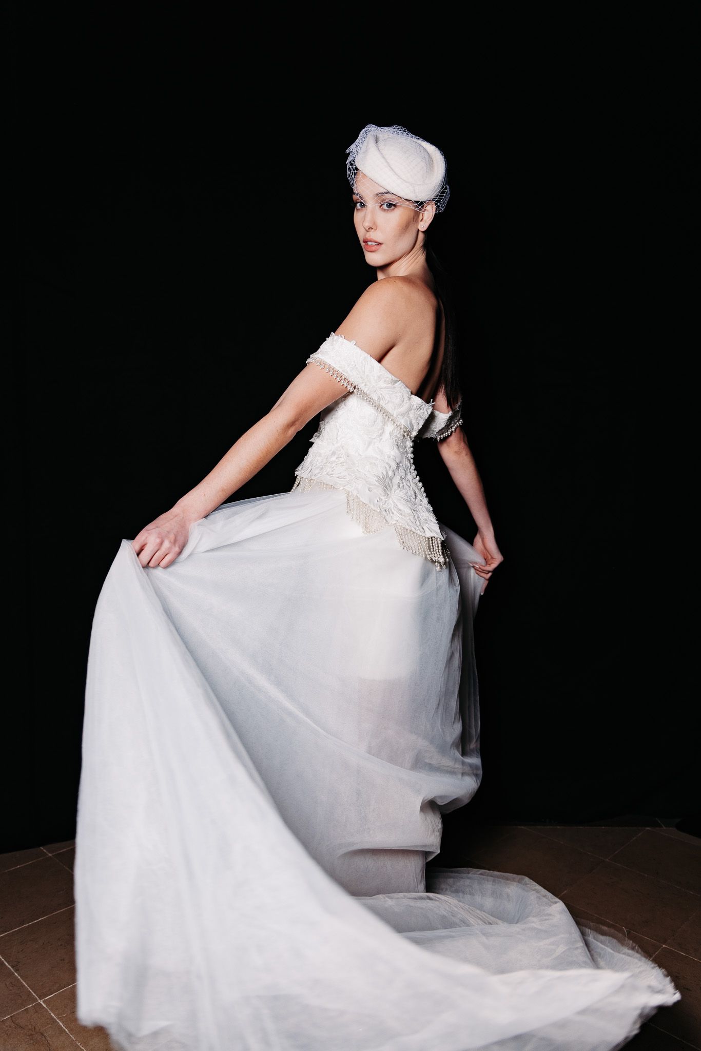 Elegant white wedding gown with off-shoulder design and flowing train photographed against dark background.