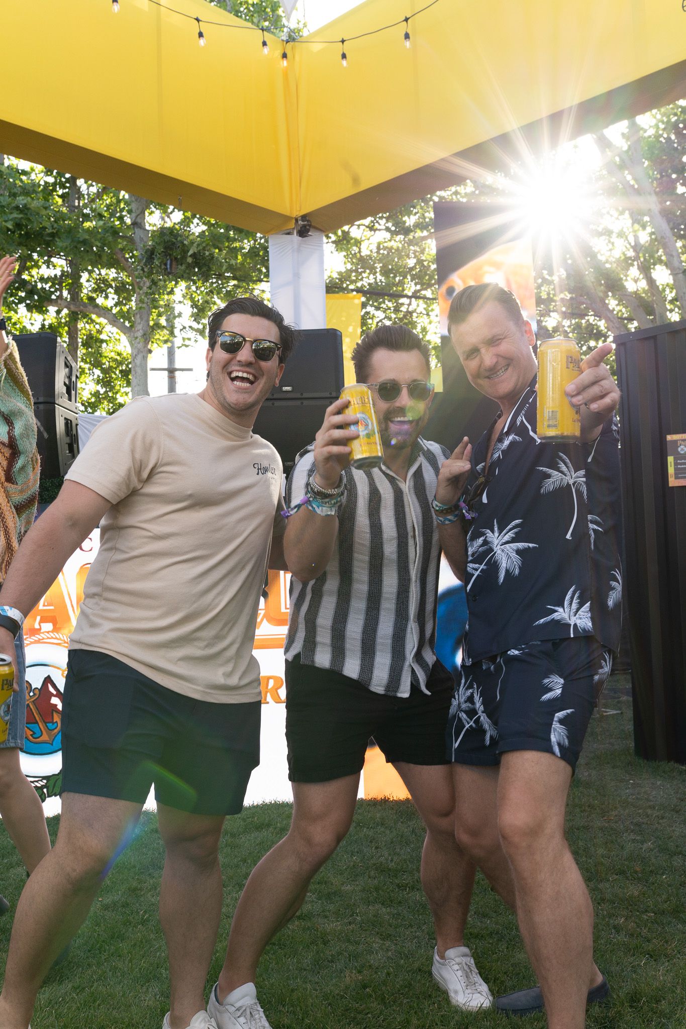 A group of friends in matching outfits hold up beverages while posing together at an outdoor summer gathering.