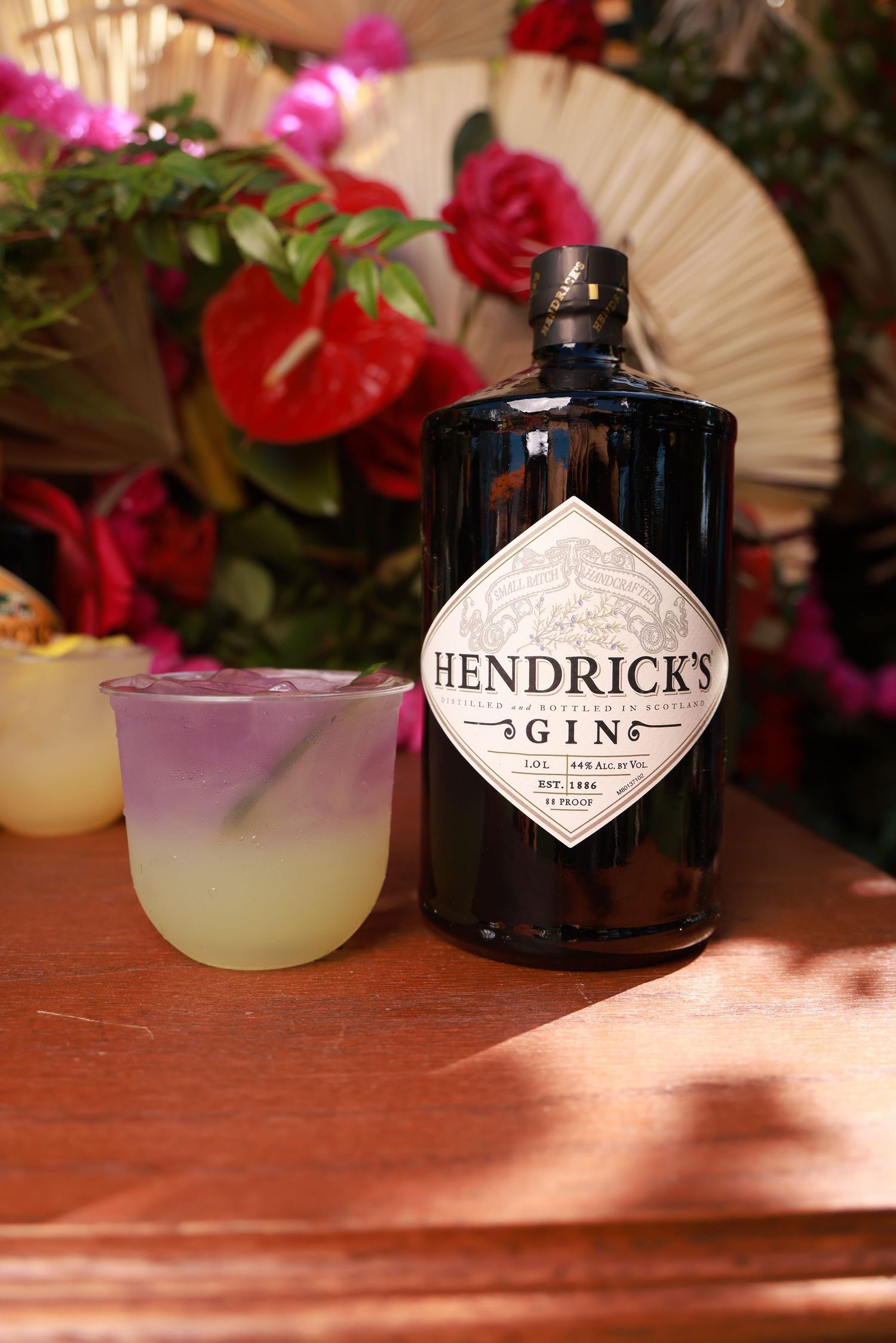 Hendrick's gin bottle displayed beside a yellow cocktail on a wooden surface with floral decorations.