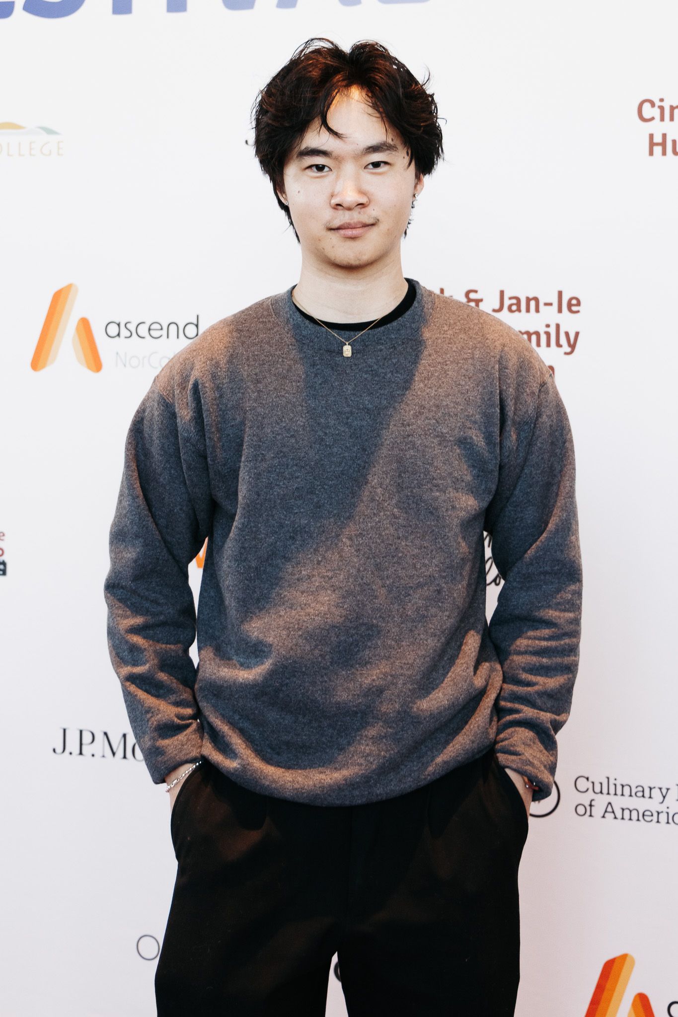 A person in a grey sweater poses against a white backdrop at a film festival.