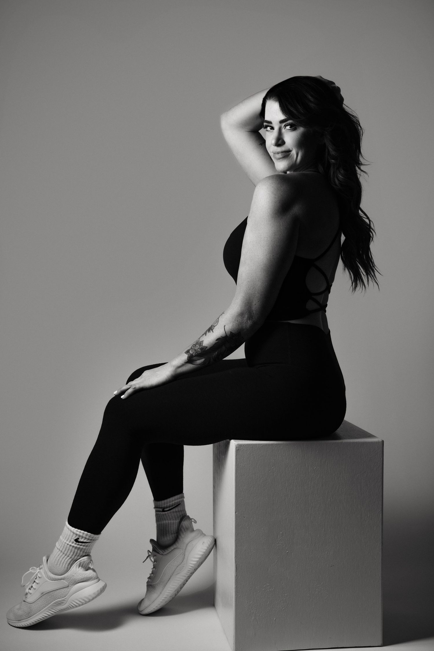 Artistic black and white photo series showing person seated on cube wearing sneakers and black clothing in dramatic lighting.