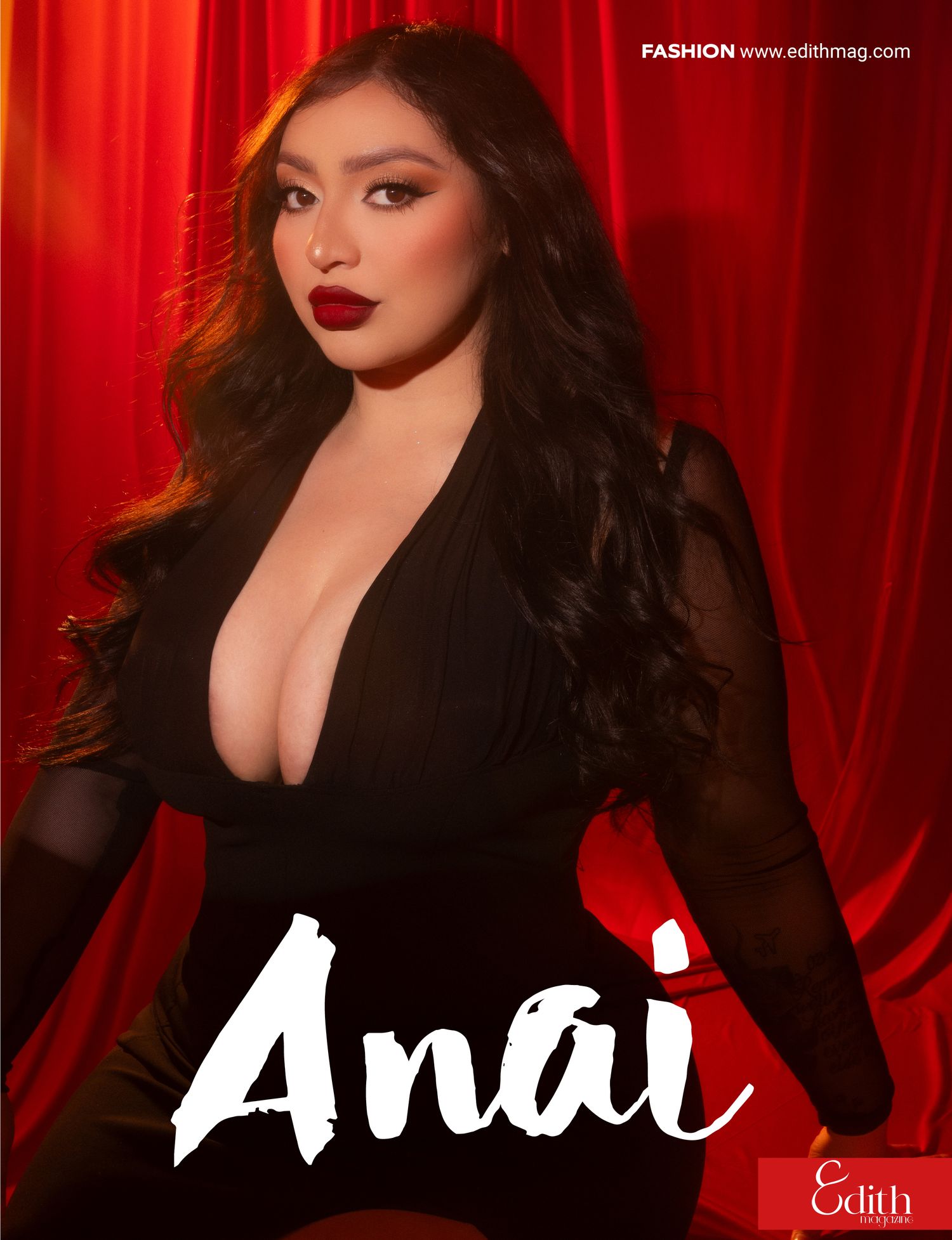 Fashion model in black dress poses dramatically against luxurious red velvet curtain backdrop.