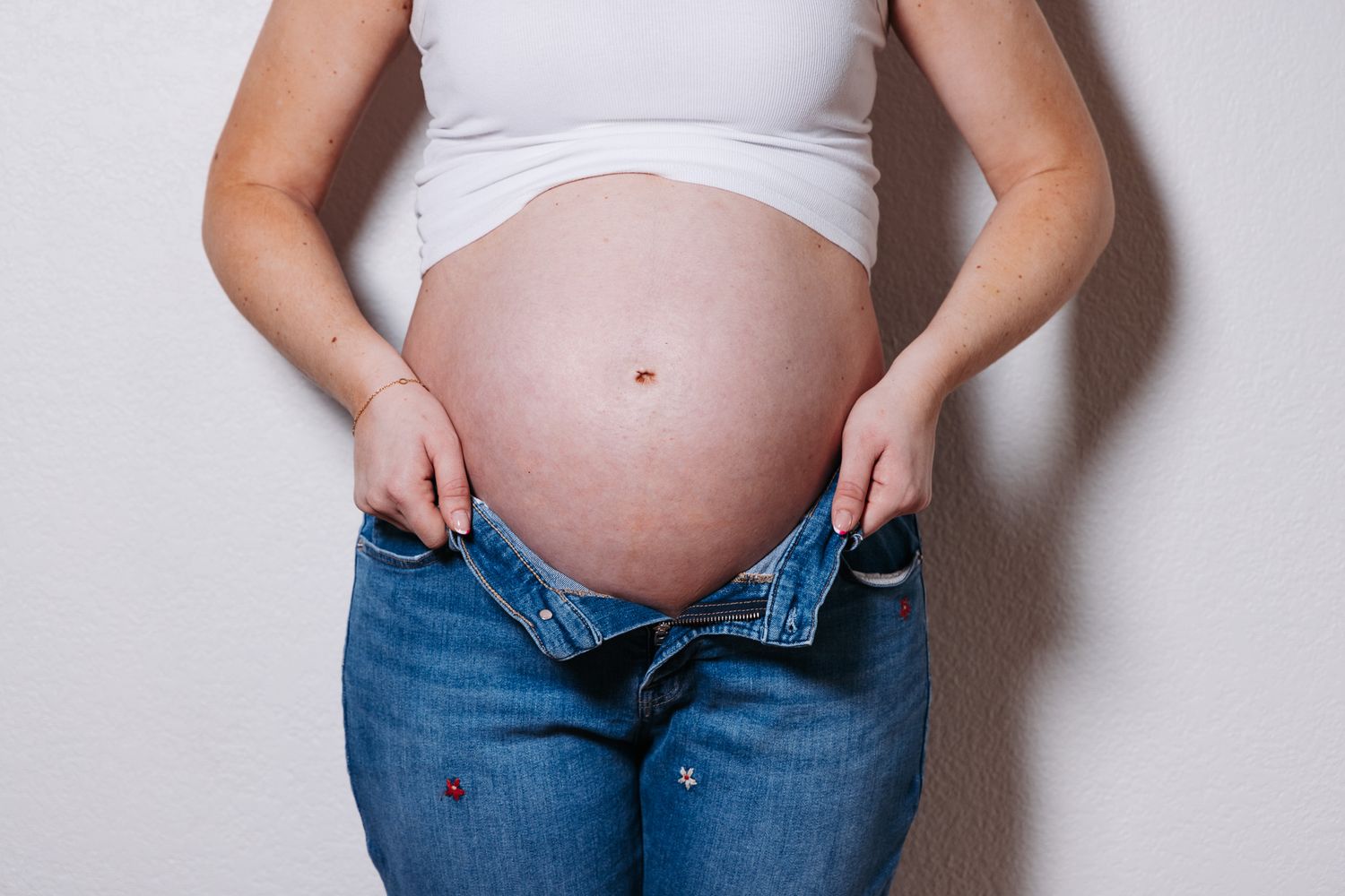 A pregnant belly is shown in stages through four photos with unbuttoned jeans against a white background.