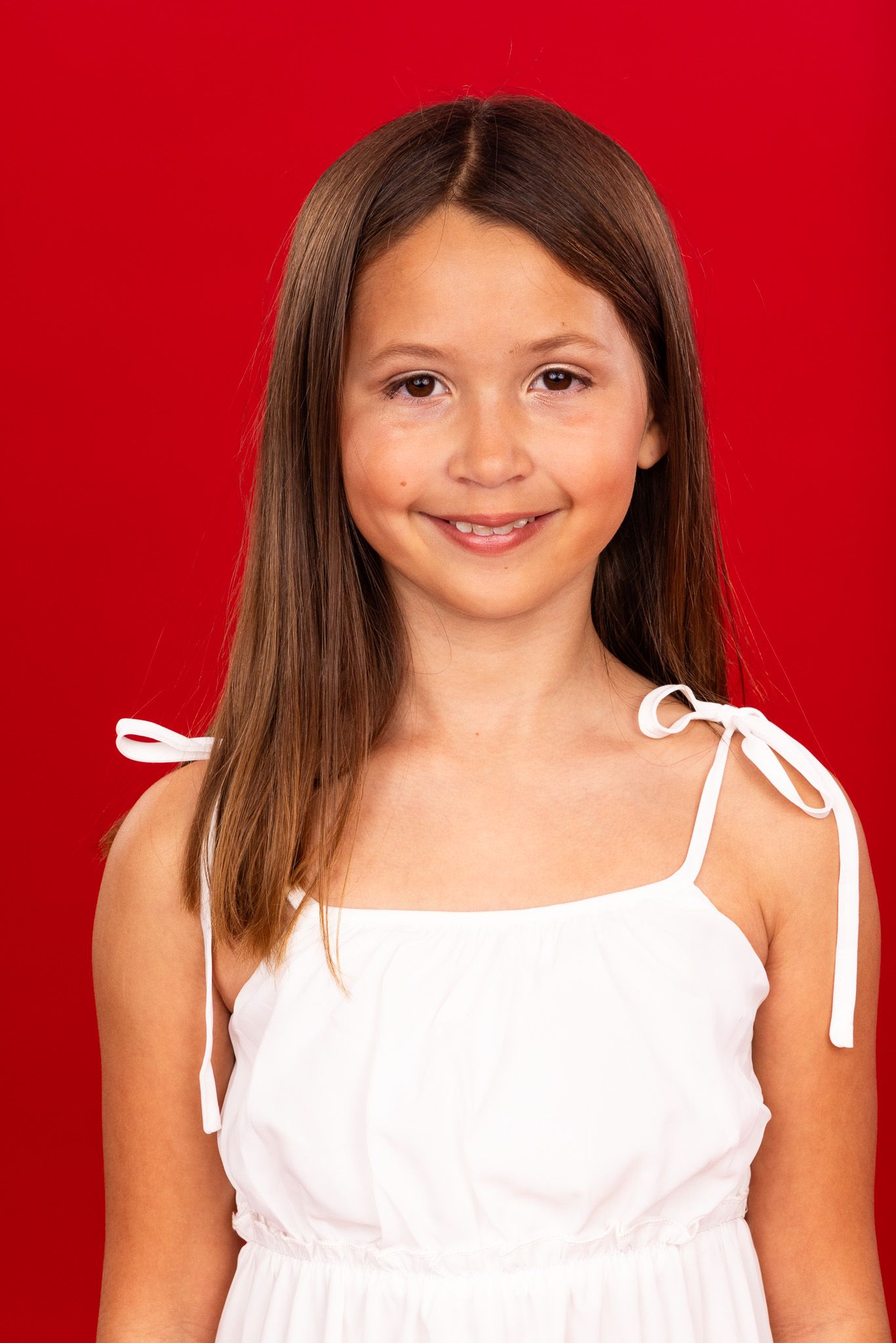 Portrait of a smiling child wearing a white sleeveless top against a vibrant red background.