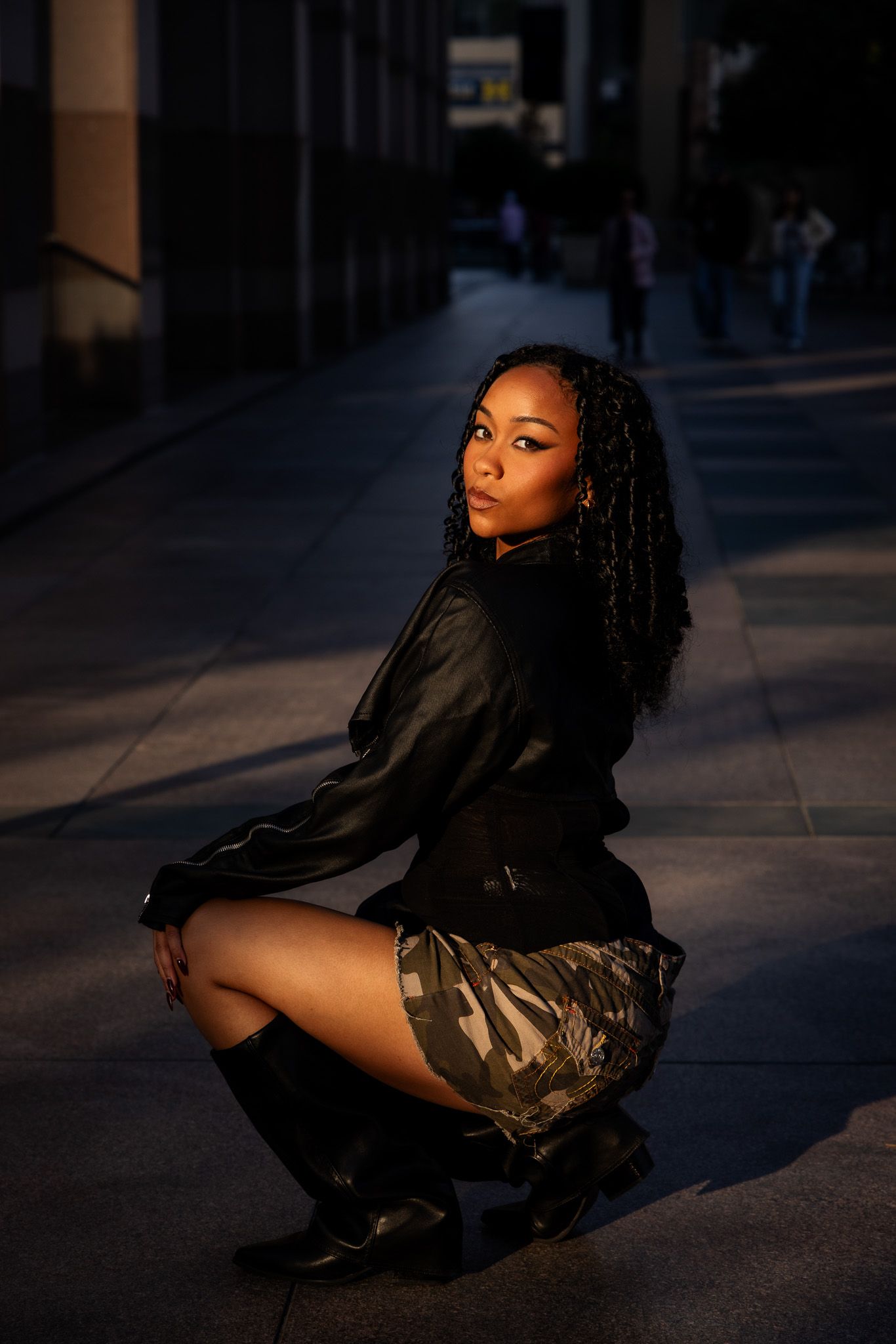 A person in a black jacket and shorts poses dramatically on the ground in moody evening lighting.