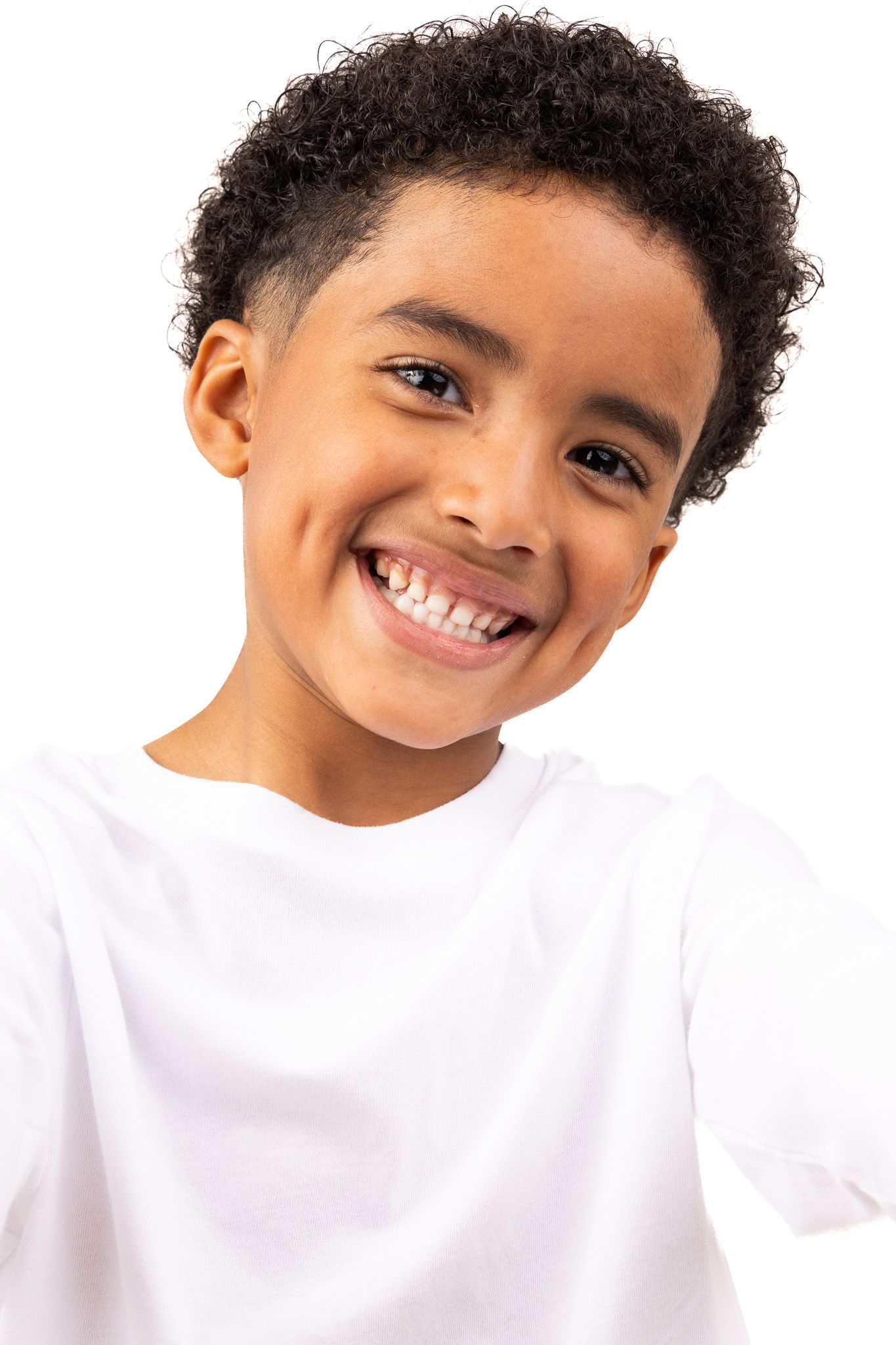 Child in white t-shirt with curly dark hair flashes a joyful smile against white background.