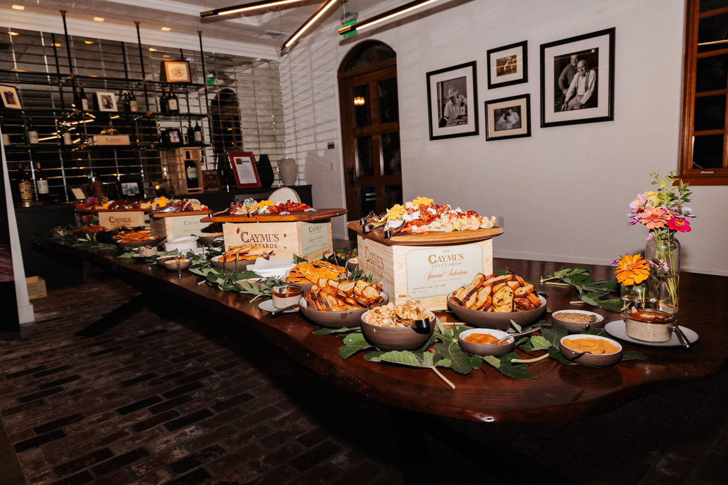 A buffet table displays various appetizers and food items in an elegant restaurant setting with framed artwork on walls.