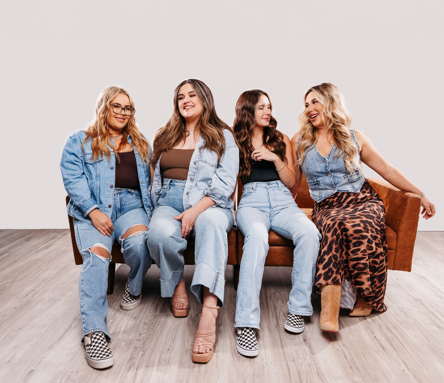 A group of friends wearing denim and casual attire sit together on a white floor, showing off their stylish footwear.