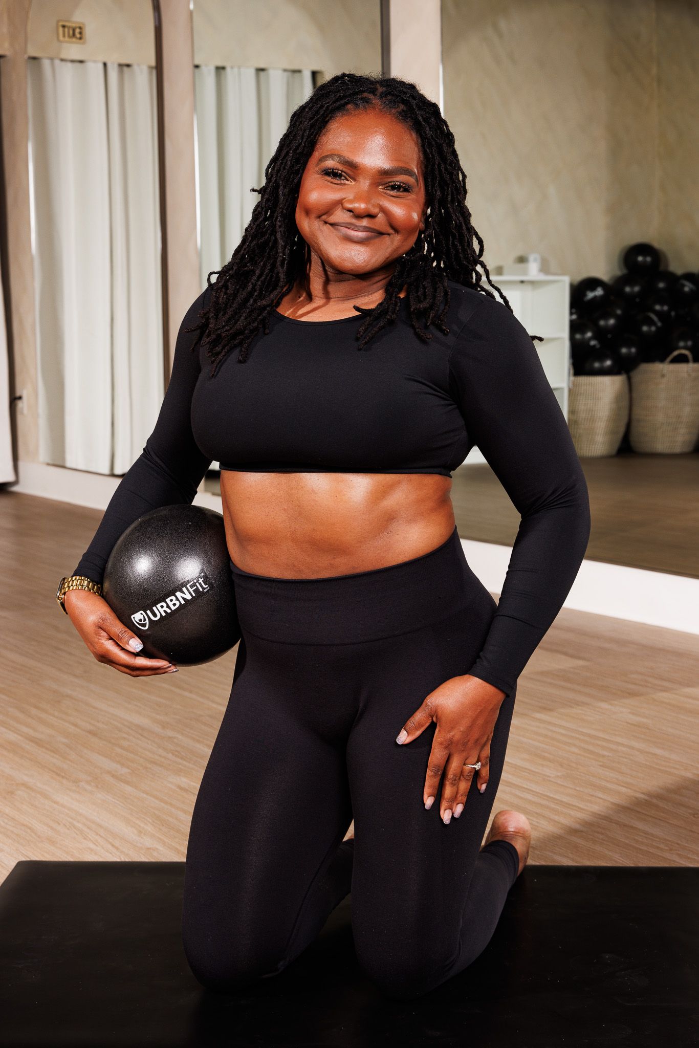 Smiling woman in black activewear holding an URBNFit medicine ball in a gym.