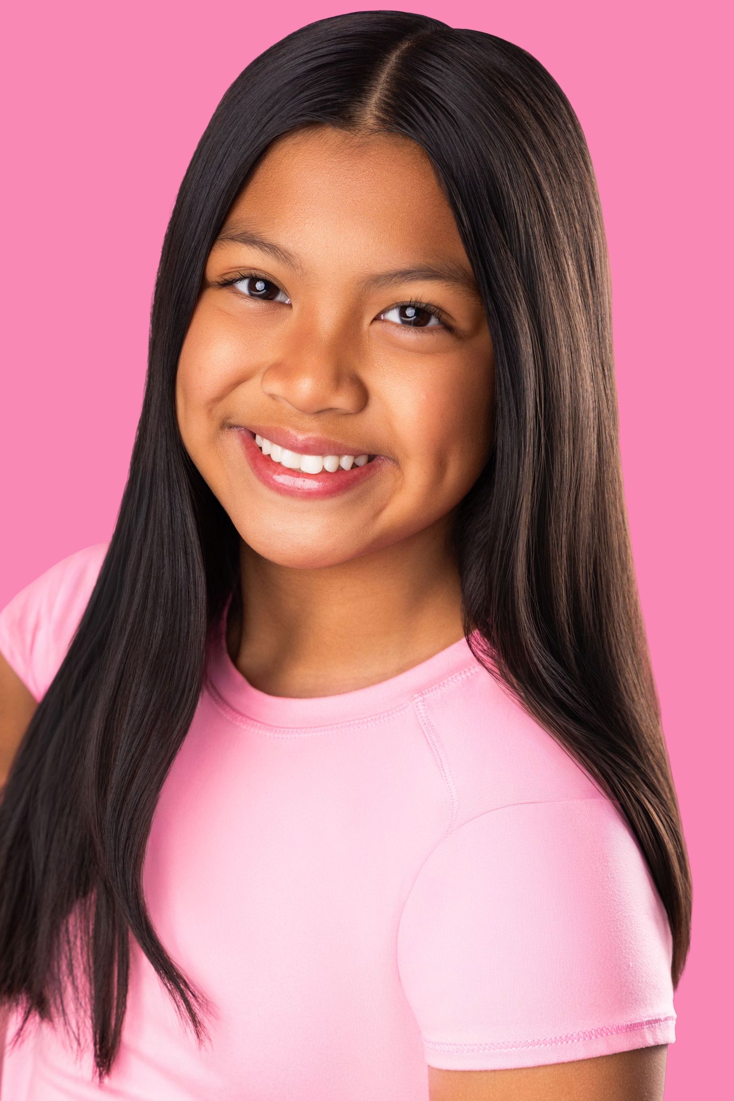 Portrait of a young Asian model with long black hair wearing a pink t-shirt against a pink background.