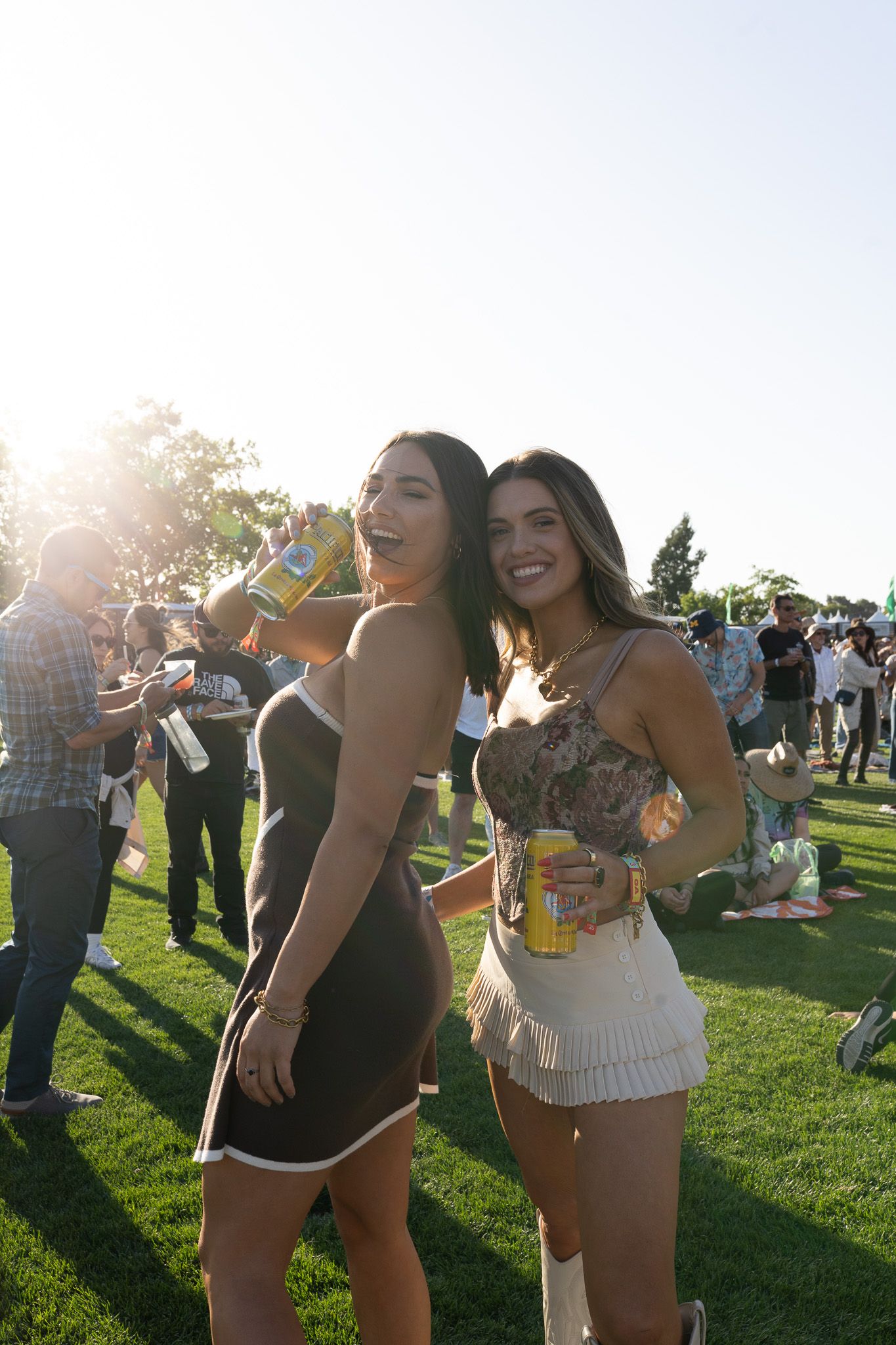 Festival goers enjoying a sunny outdoor event on a grassy field during sunset.