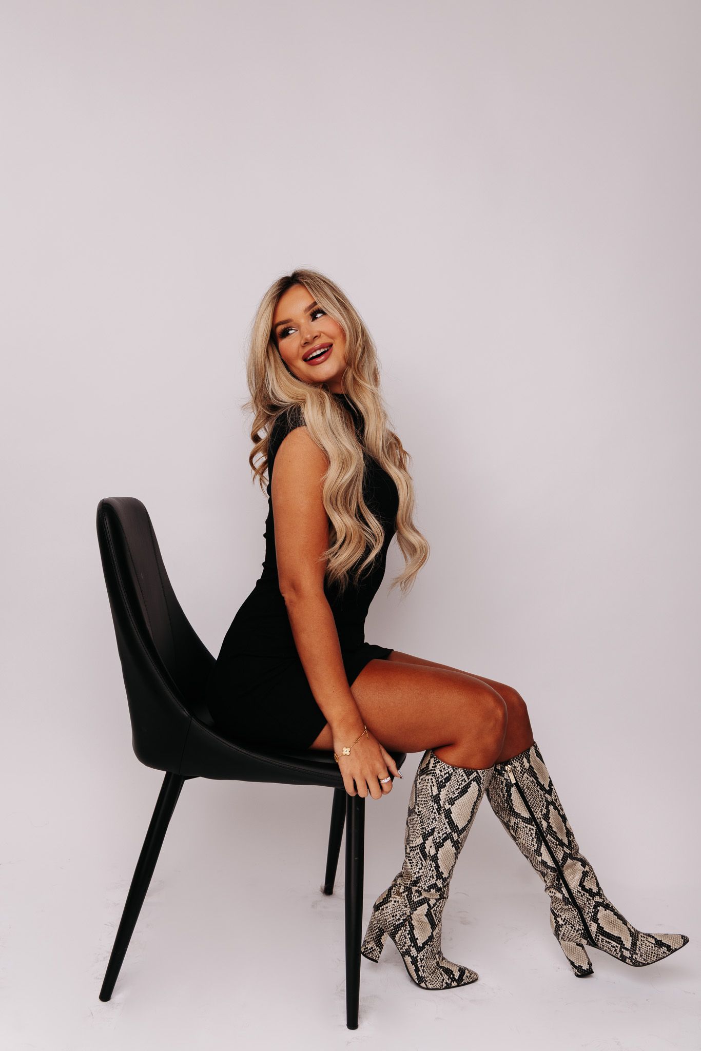 A fashion photo series showing a model in snakeskin boots posing on a black chair against a white backdrop.