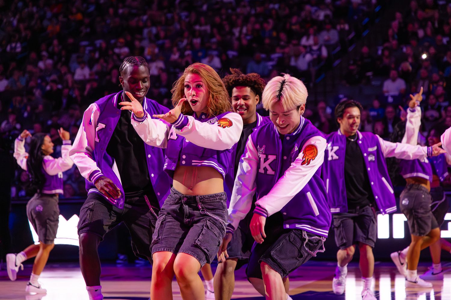 Energetic dancers perform in purple varsity jackets during NBA Sacramento Kings halftime show.