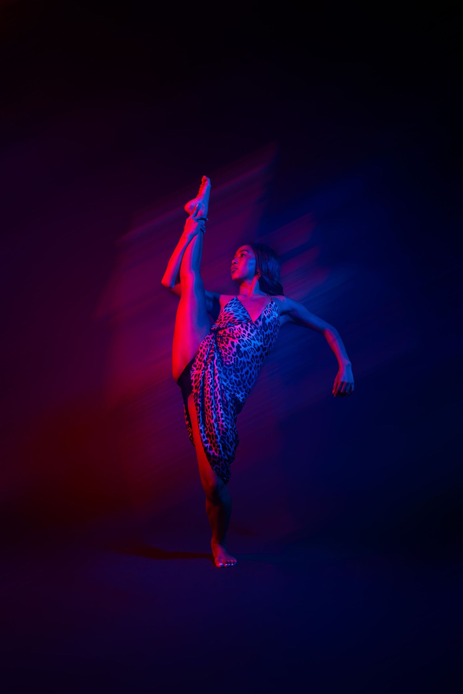 Dancer performs expressive movements in dramatic red and blue lighting creating an ethereal silhouette effect.