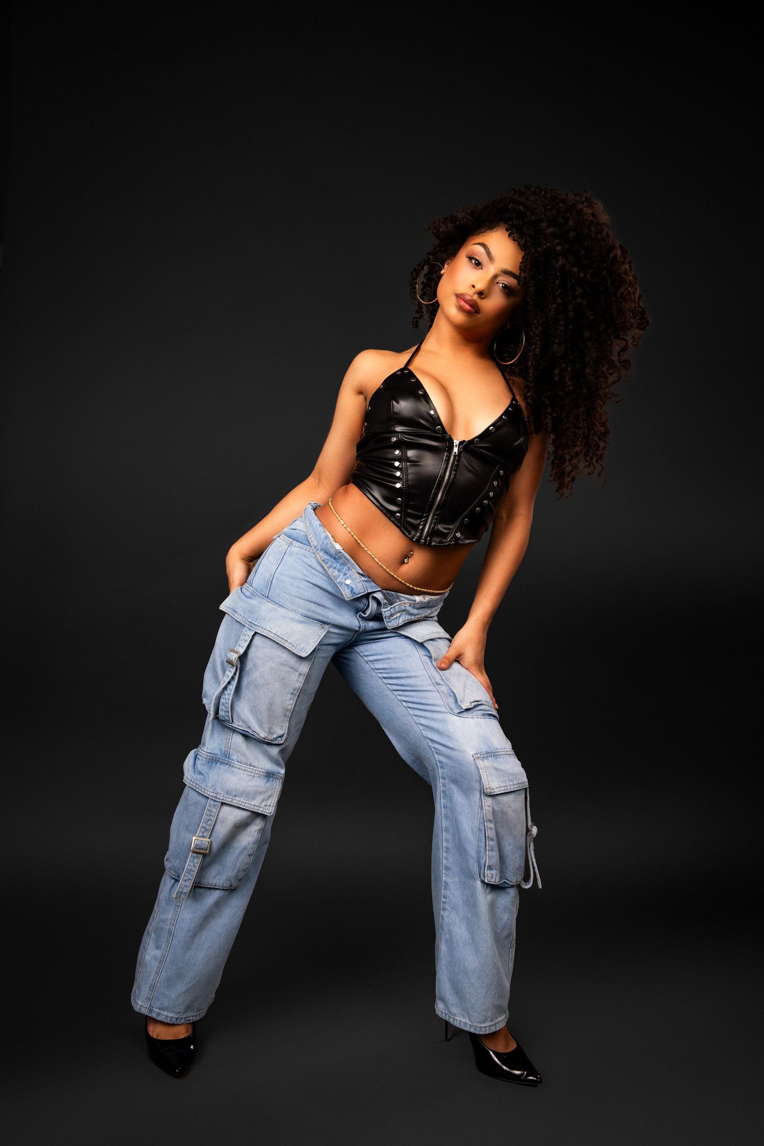 Dynamic fashion photo of model in baggy cargo jeans and black crop top dancing against dark studio background.