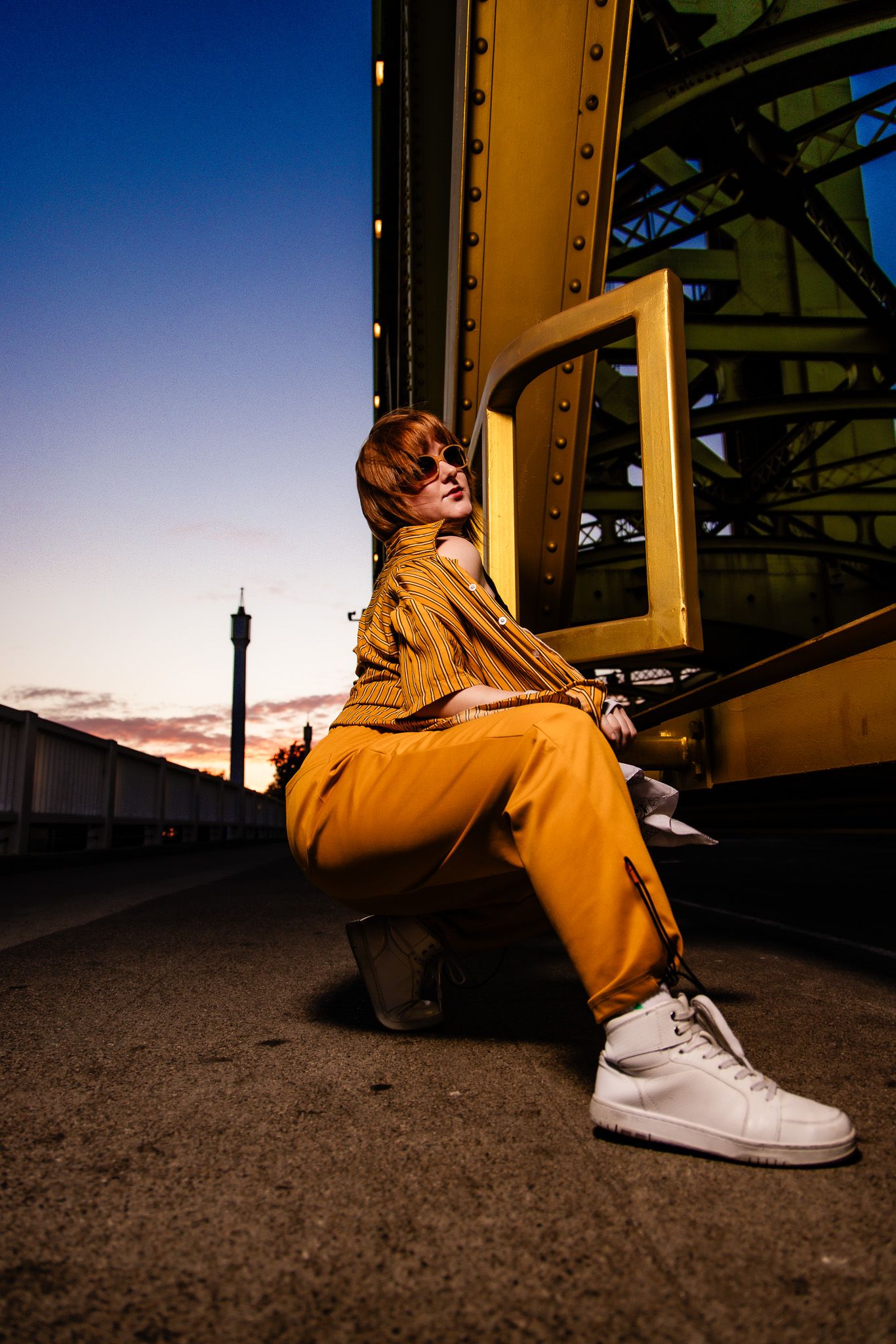 Person wearing a yellow hoodie and white sneakers sits against a metal structure during sunset.