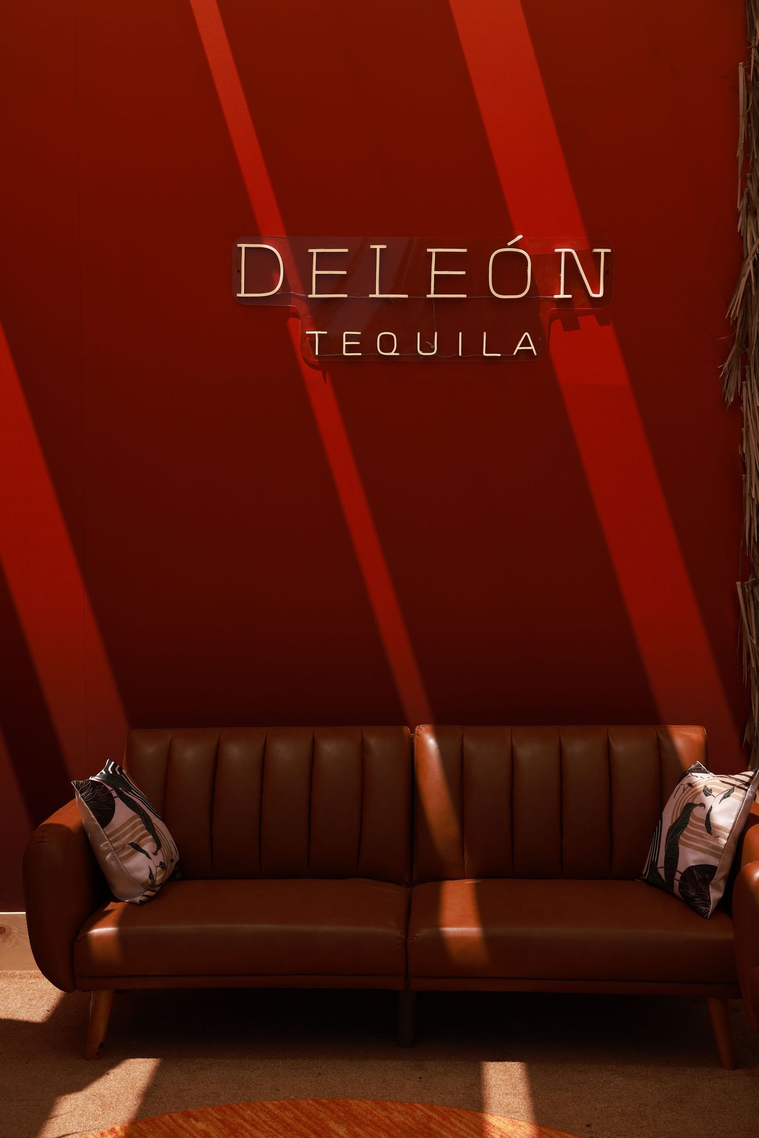 Dramatic lighting creates diagonal shadows across a brown leather booth with DeLeon Tequila branding in a dimly lit space.