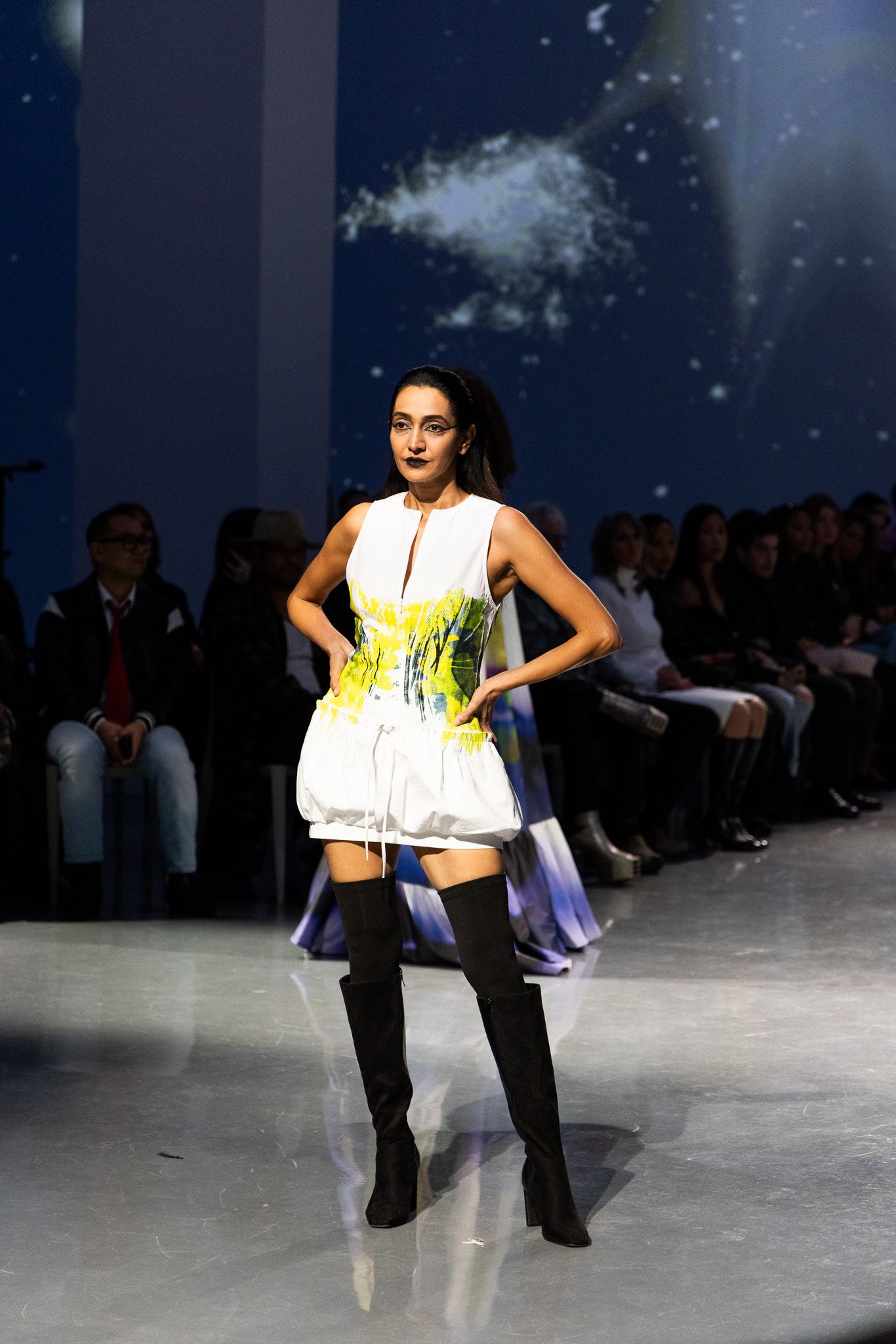 Fashion models showcase avant-garde white crop tops and dark pants on a dimly lit runway.