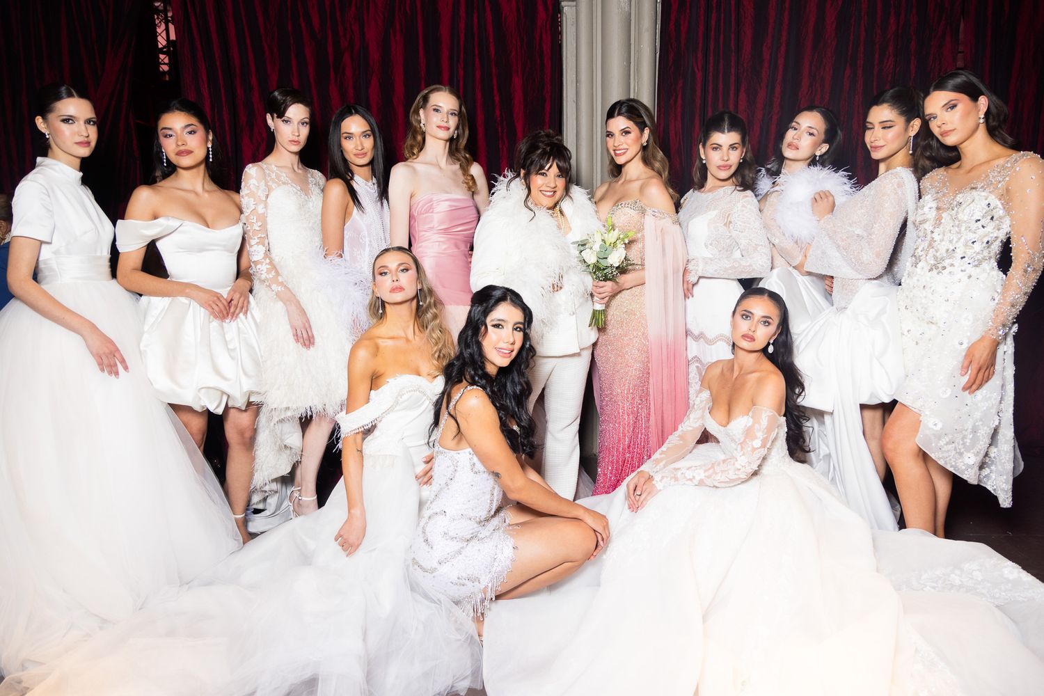 A group of women in white dresses pose together at a formal event in an elegant setting.