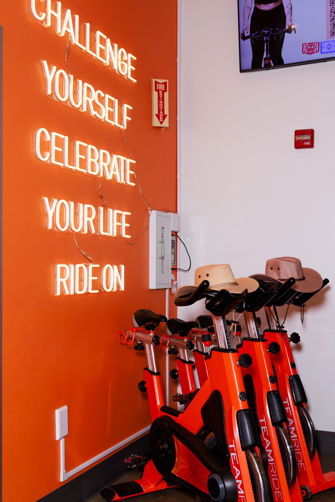 Orange spin studio with neon motivational quote and stationary bikes topped with cowboy hats.