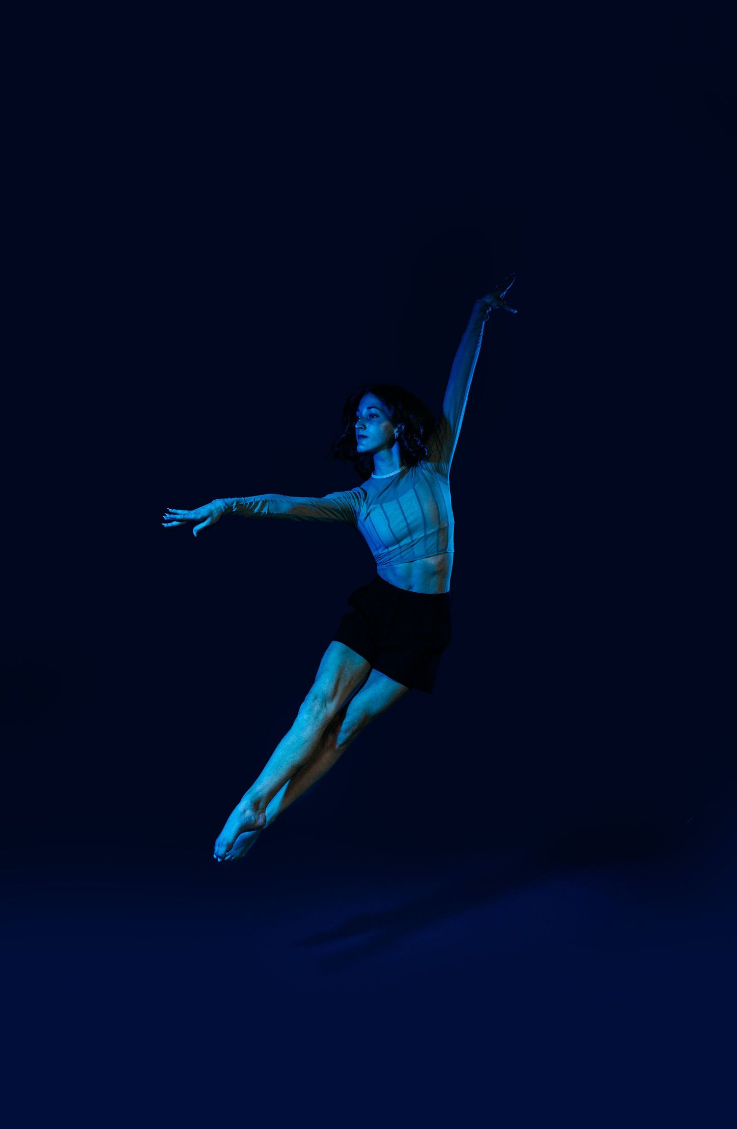 Dancer leaping through dark space illuminated by blue theatrical lighting.