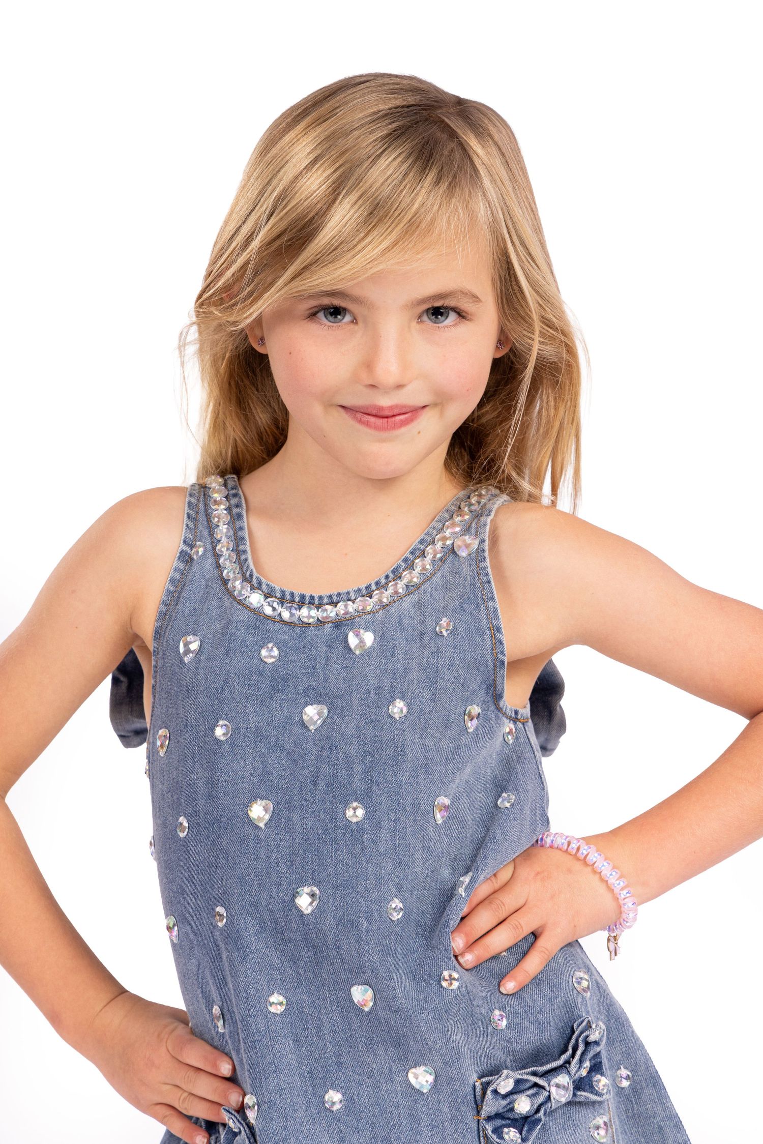 Child wearing a sleeveless denim dress with white heart pattern embellishments and bow detail.