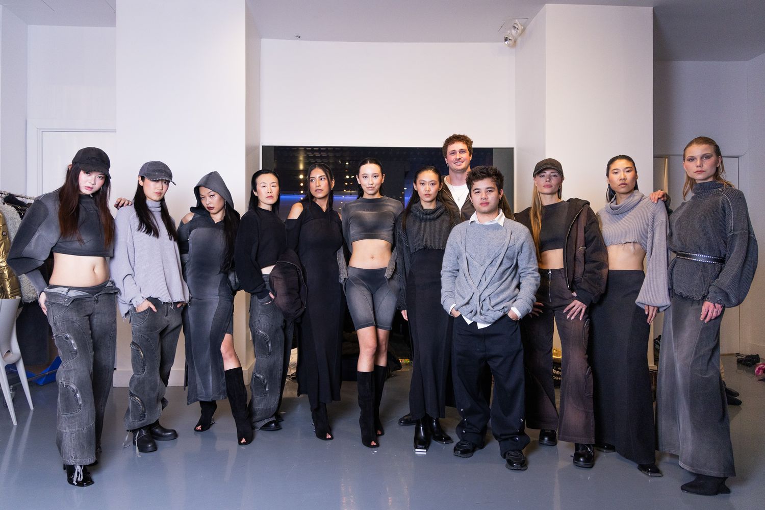 Fashion models lined up along white studio wall in casual clothing and boots.