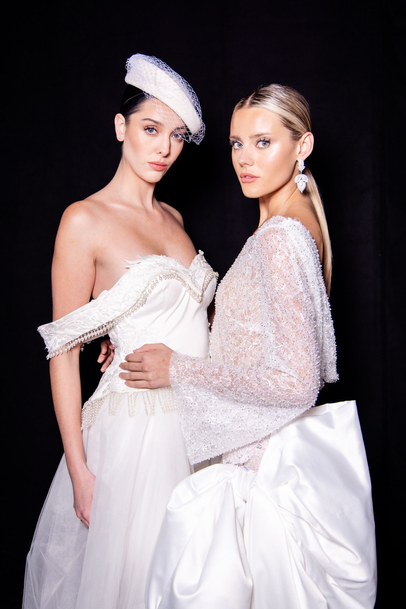 Two models showcase elegant white bridal gowns with sequined details against a dark backdrop in fashion photography.