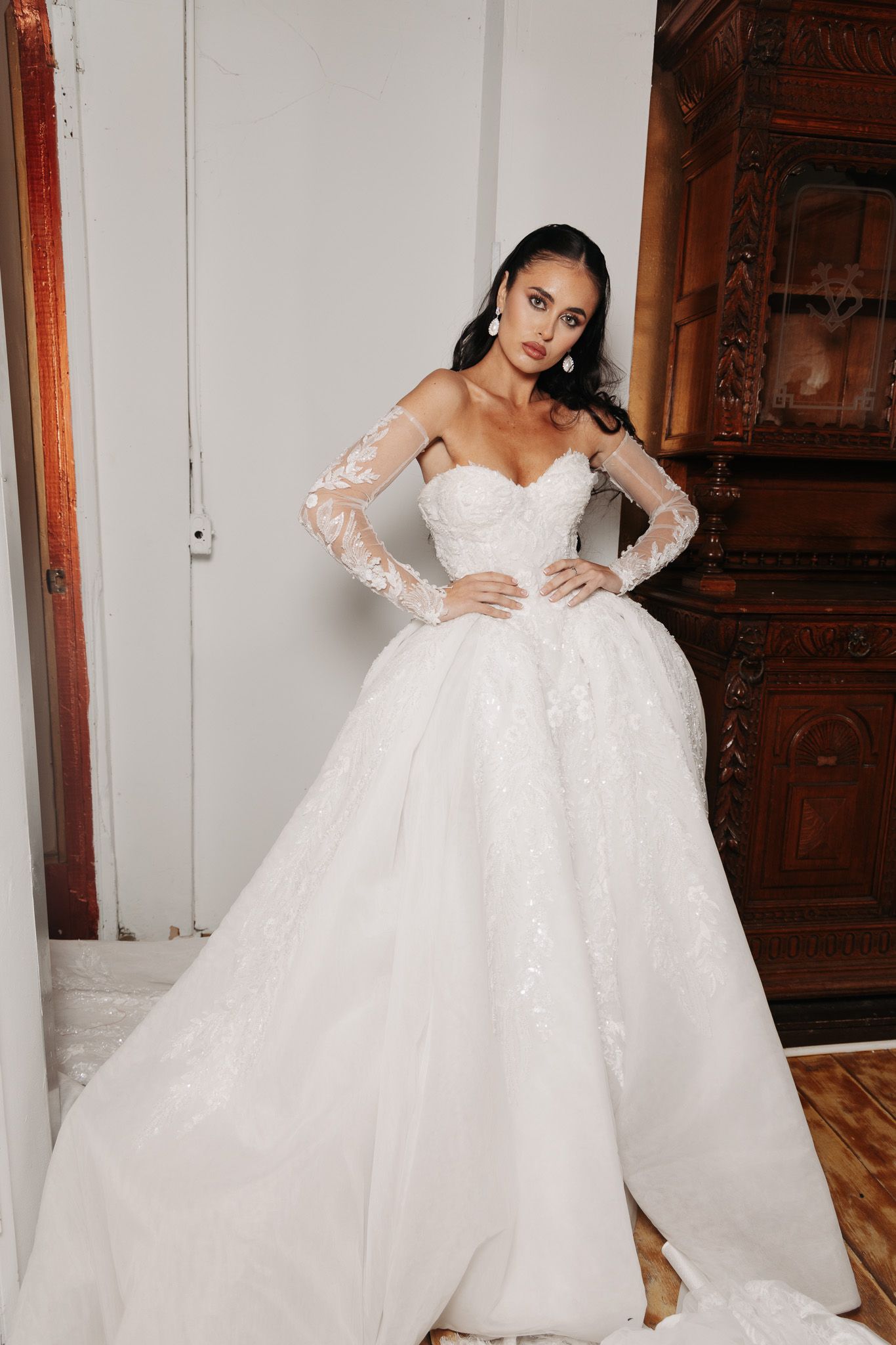 Elegant ball gown wedding dress with lace sleeves and sweetheart neckline posed against wooden decor.