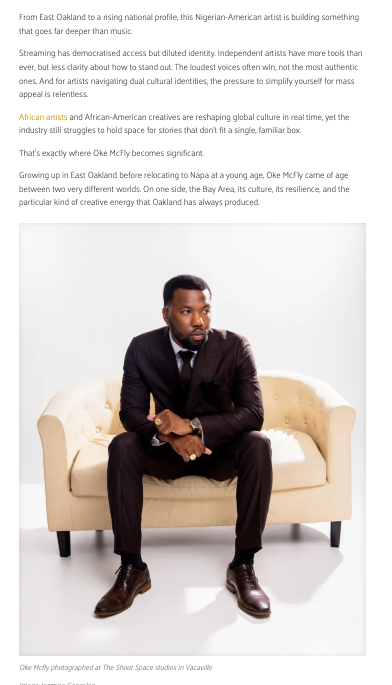 Nigerian-American artist Oke McFly sits confidently on a cream sofa in a sharp black suit at The Shoot Space studio in Vacaville.