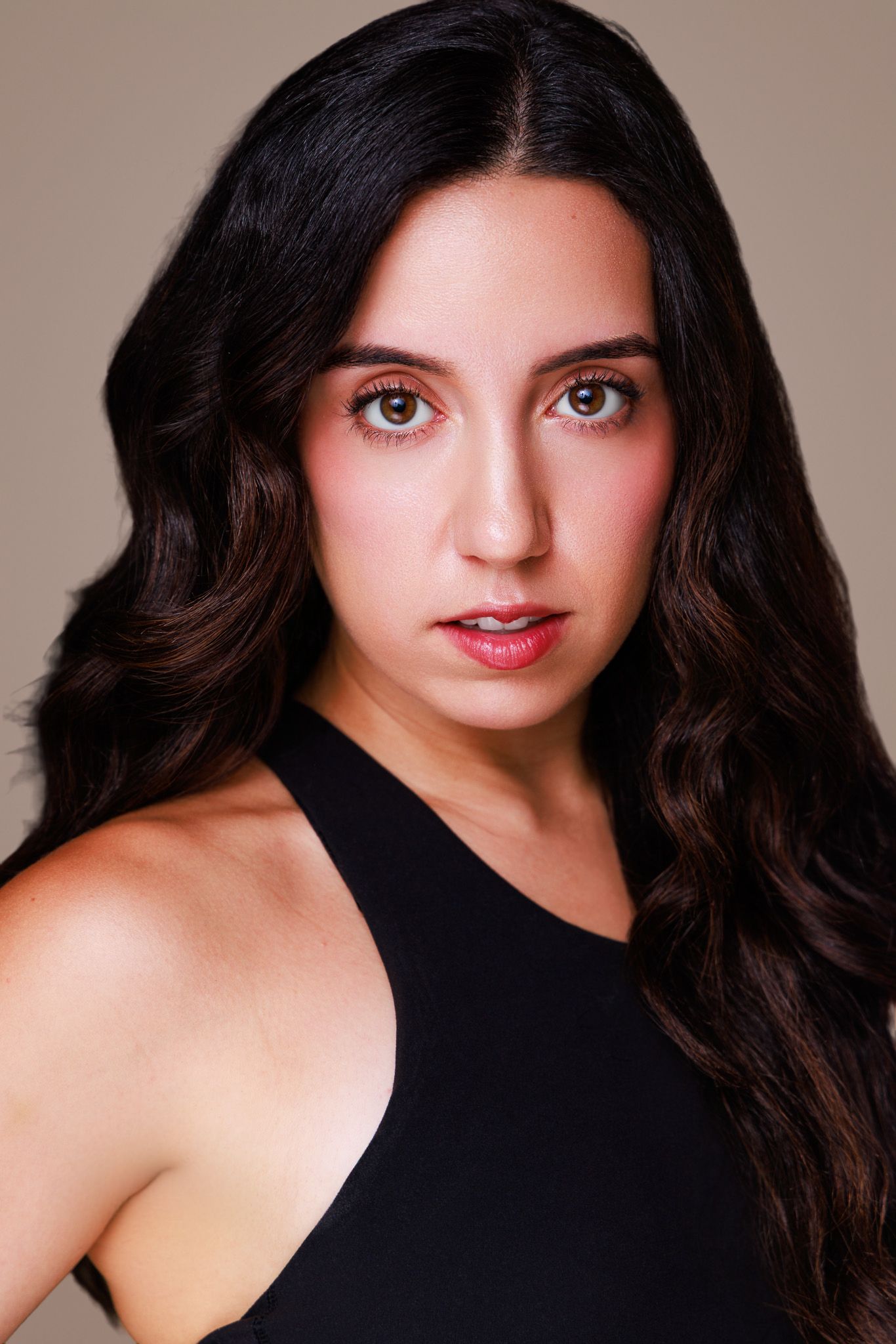 Young woman with long dark wavy hair and green eyes wearing a black top, professional headshot portrait.