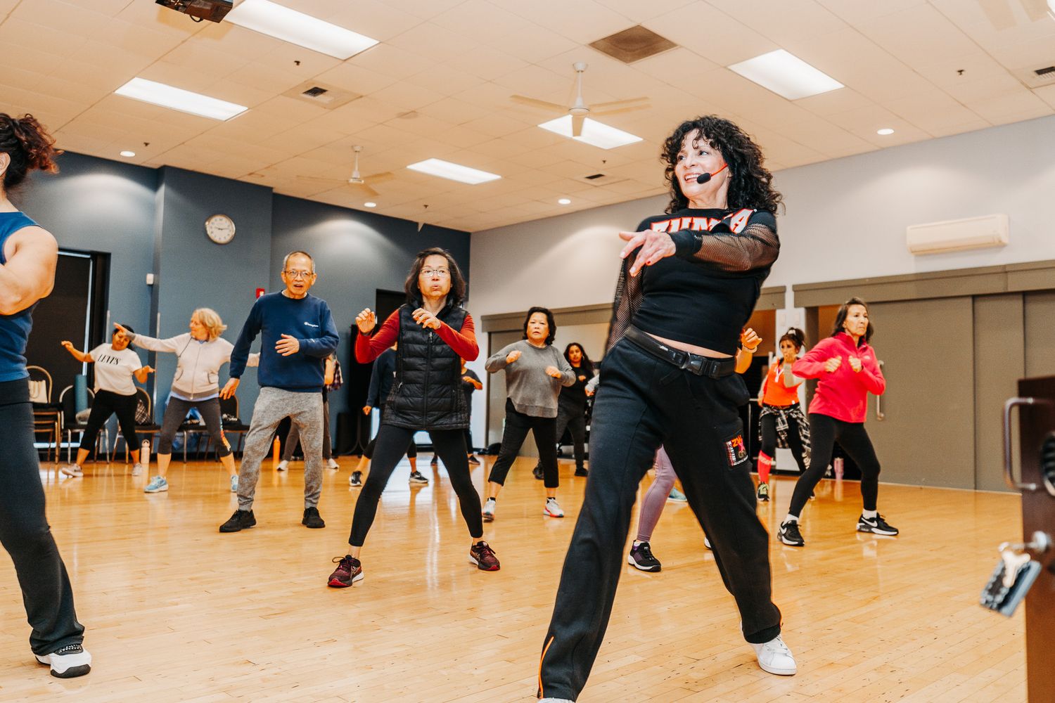 Group exercising in a bright dance studio during a dance fitness class.
