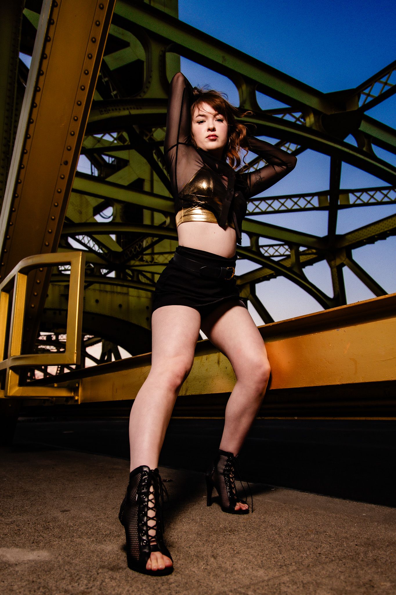 A close-up series of black heeled shoes against a bridge structure background during golden hour lighting.