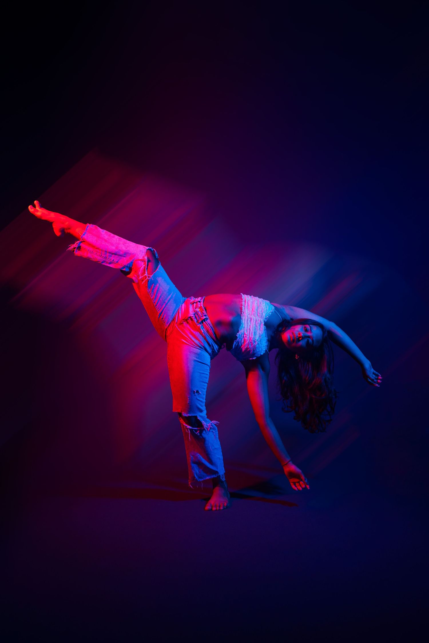 Dynamic performance art featuring a dancer in red and blue lighting creating flowing movements against dark backdrop.