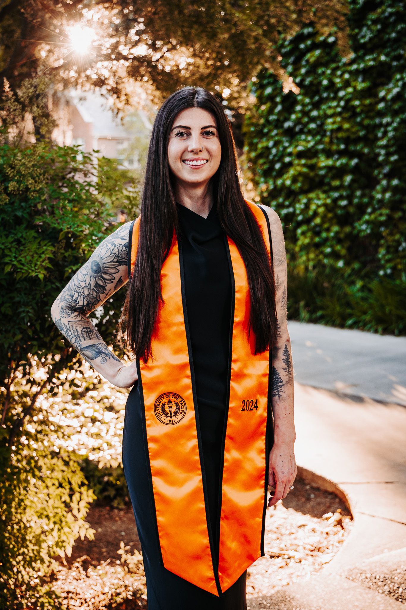 Graduation portrait series showing a graduate in black gown and orange stole against a sunny outdoor backdrop with ivy.