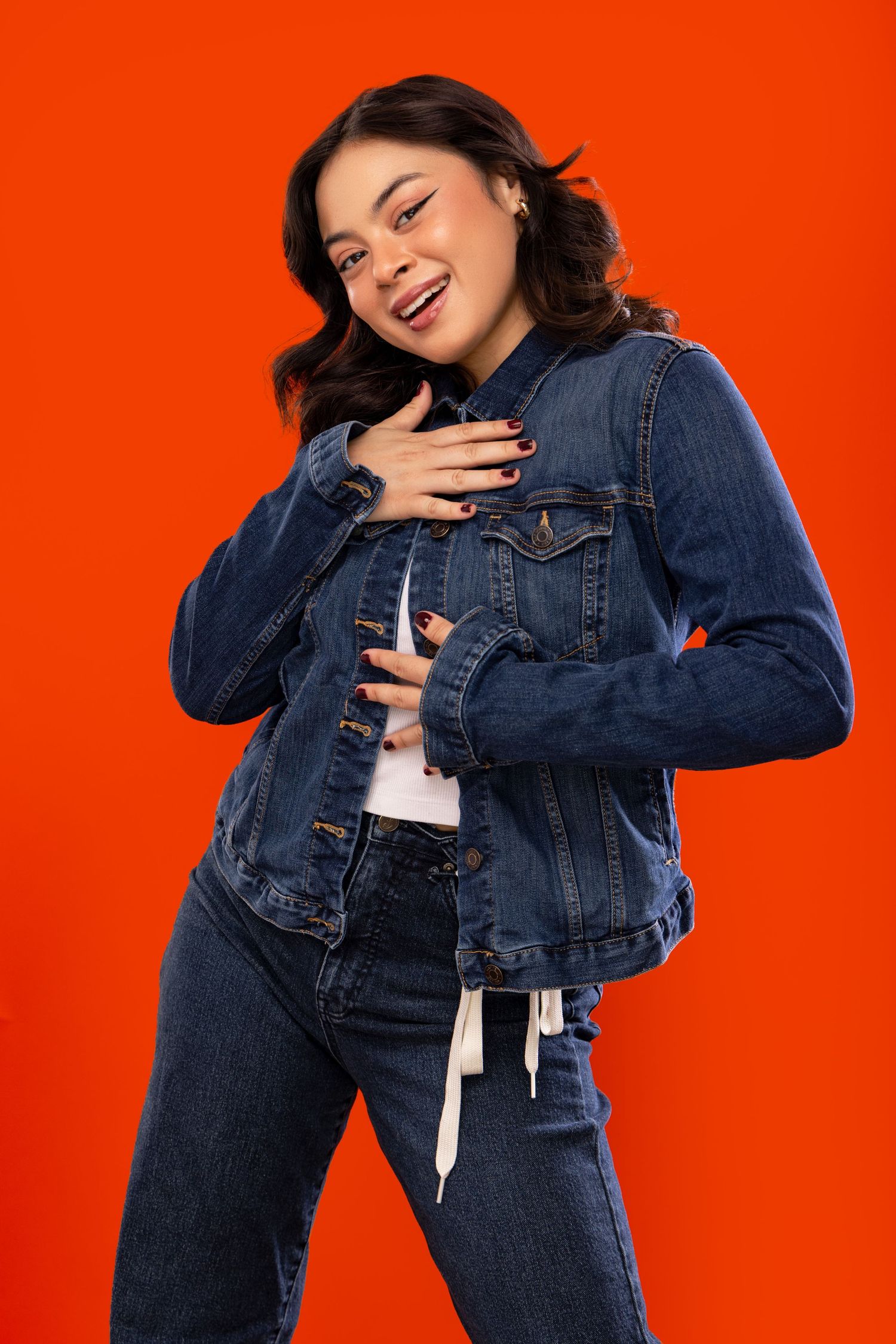 Woman posing playfully in denim jacket against bright orange background in sequential lifestyle photoshoot.