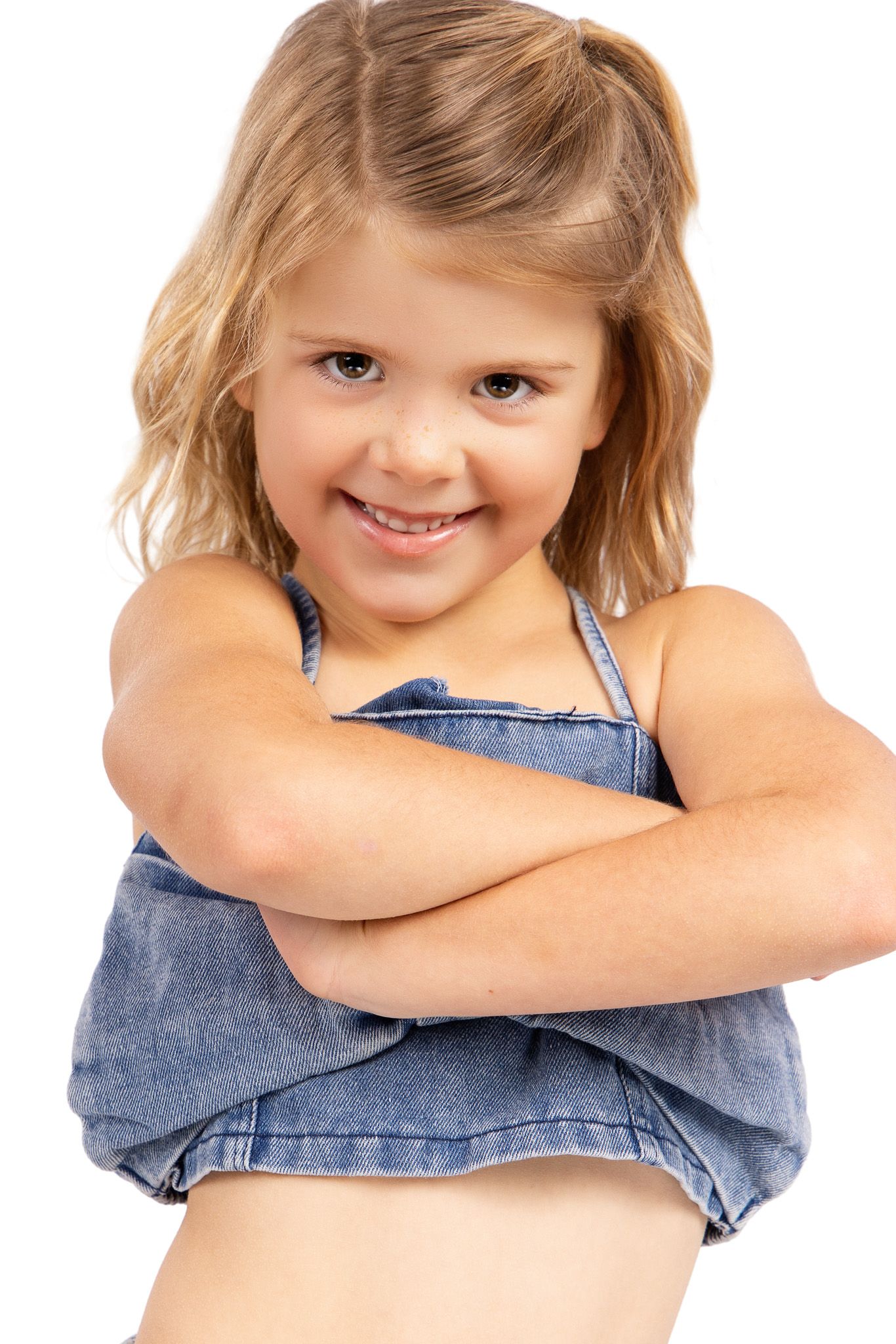A child in denim overalls smiles and poses playfully against a white background.