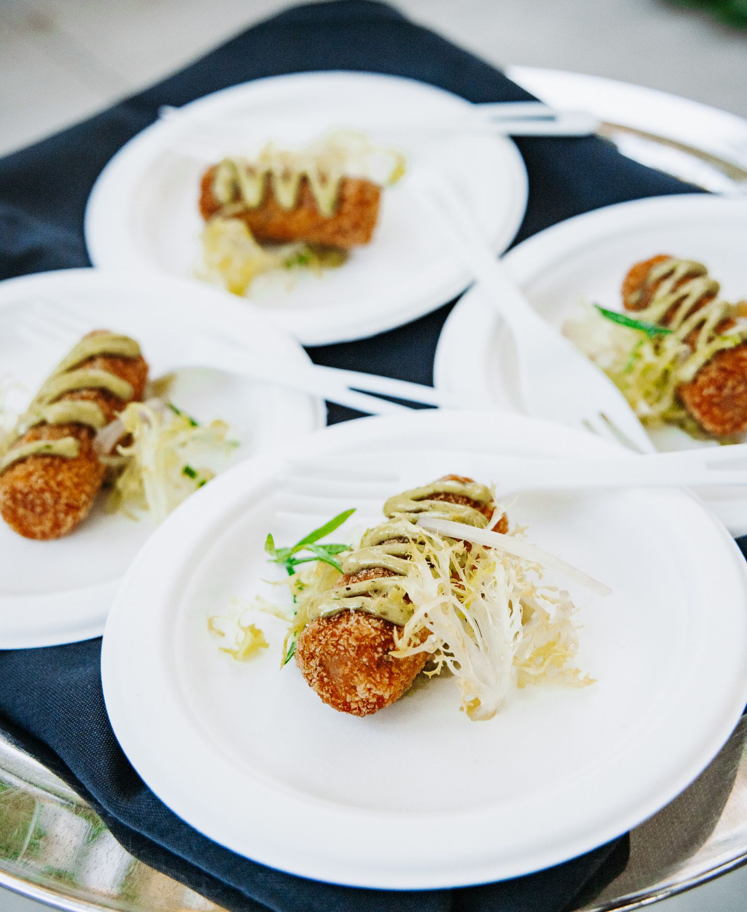 Several small plates of appetizers with garnishes arranged in a row on a dark surface.