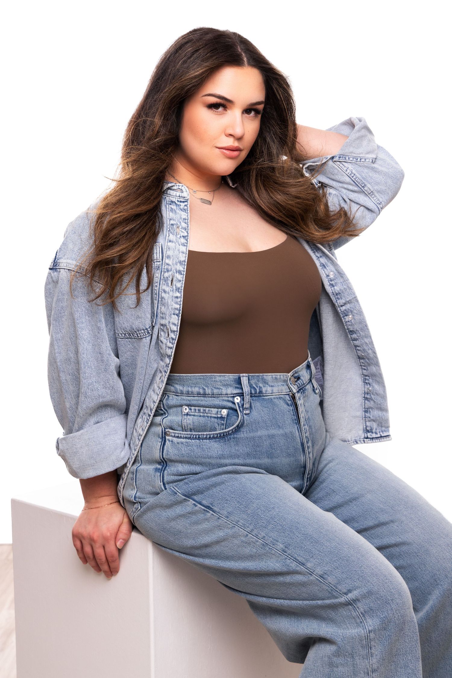 Model poses in casual denim overalls and brown top against white background in fashion photography series.