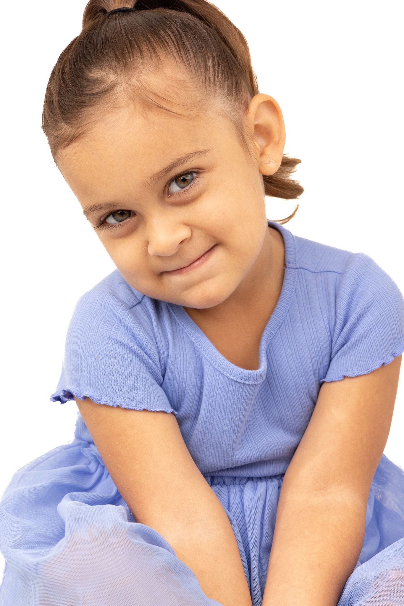 Young child in a light blue dress smiling sweetly while sitting in a casual pose.