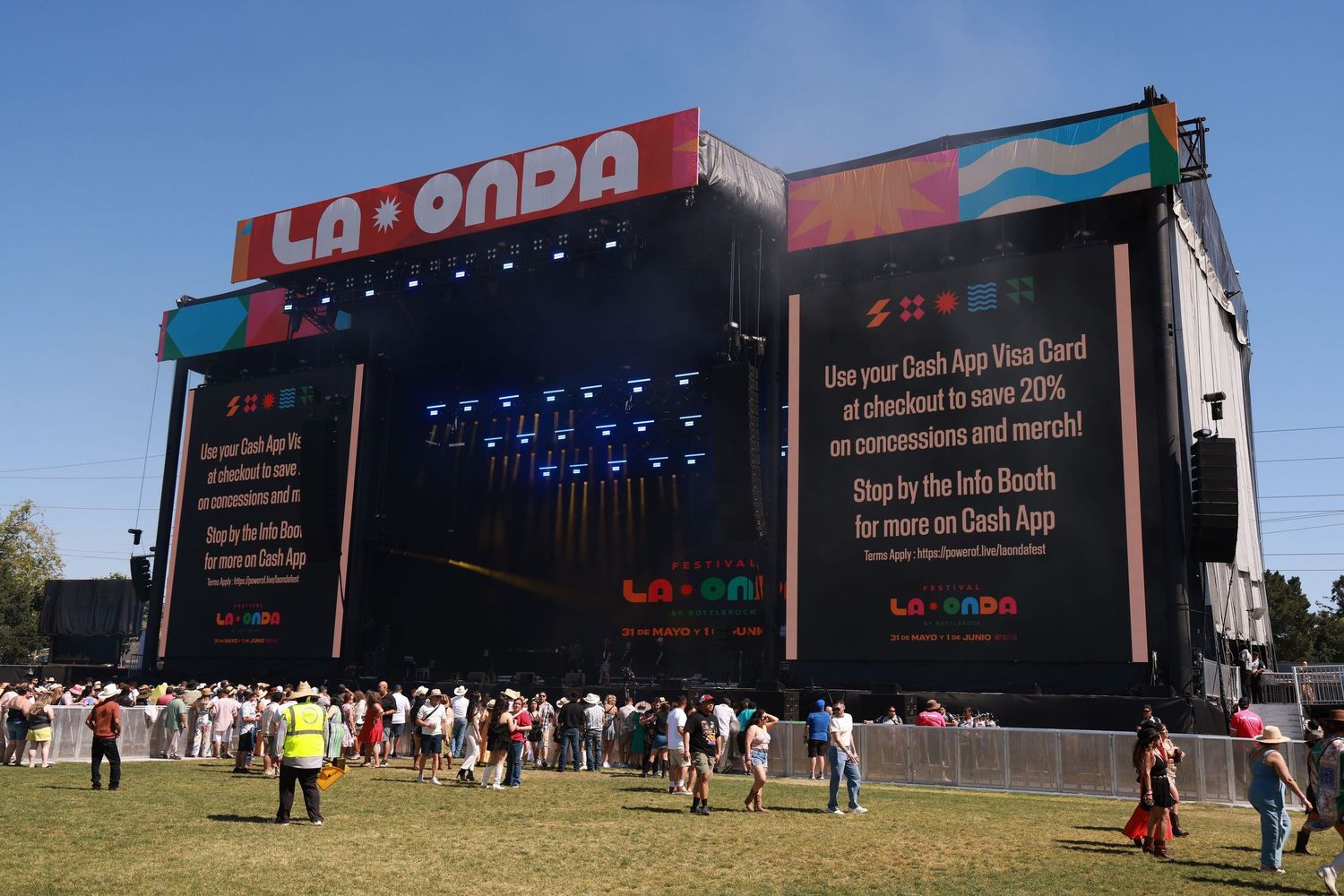 Large outdoor festival stage with LED screens and 'La Onda' signage as crowds gather during daytime.