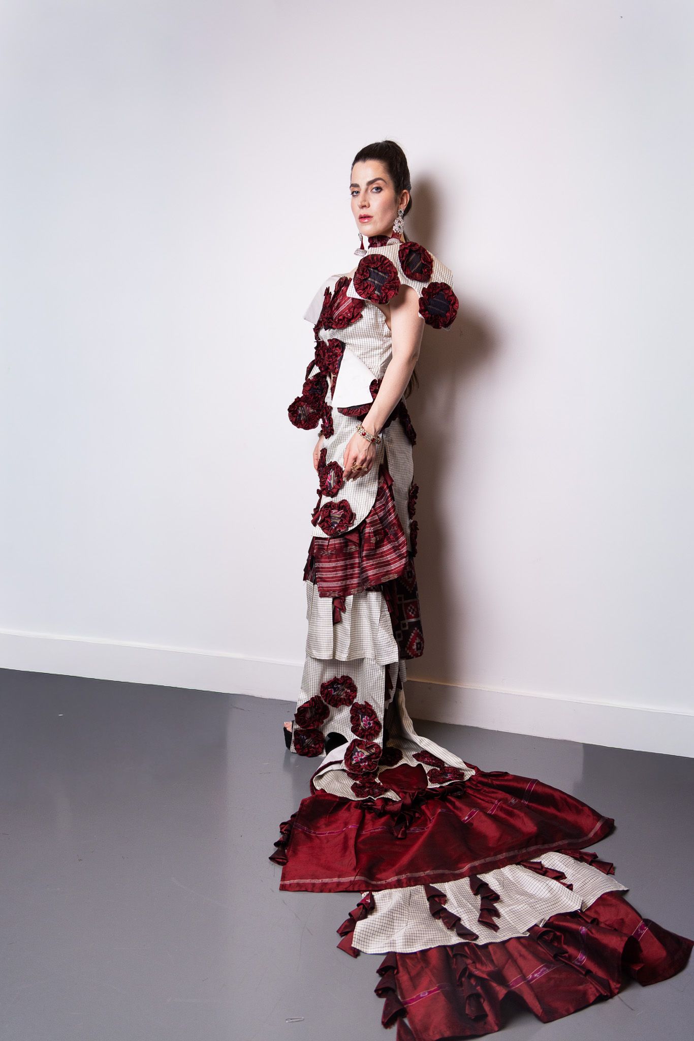 Model wearing avant-garde red and white ruffled gown in minimalist studio setting.