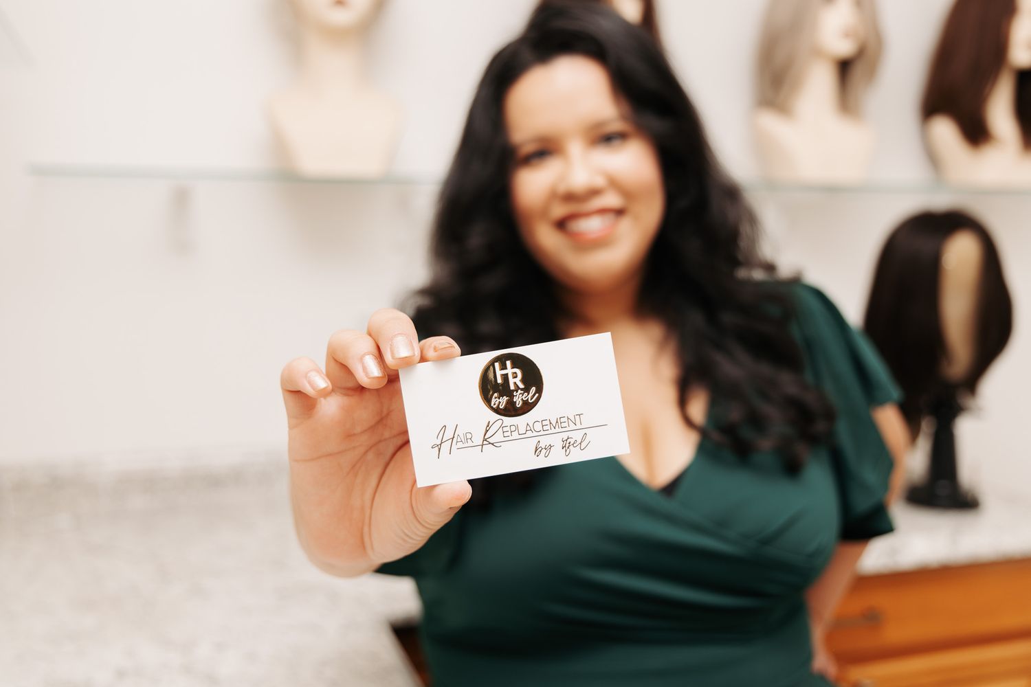 Person in a dark green top smiling and showing a business card in a professional setting.