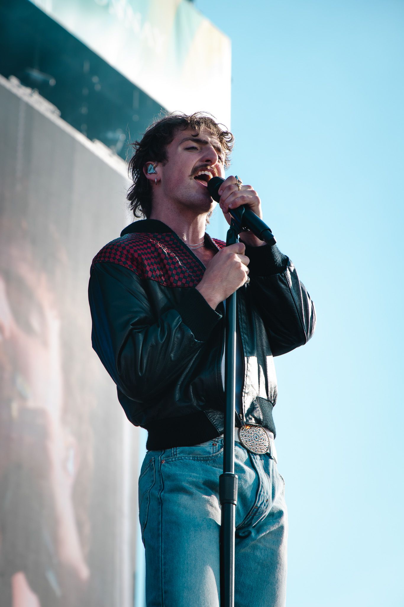 Singer performs passionately on stage in dark lighting wearing blue jeans and black jacket.