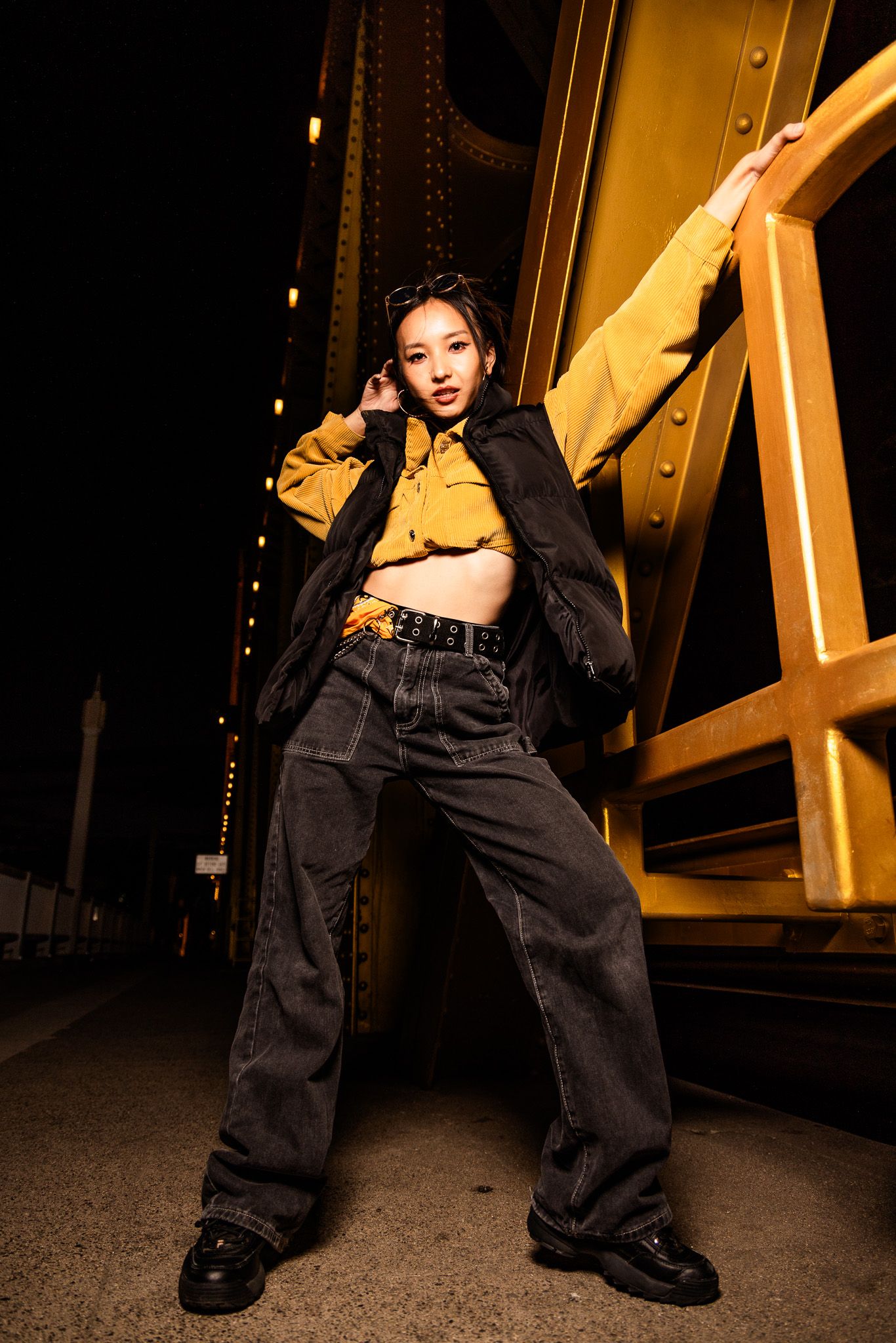 Low angle view of a person in baggy black pants and boots against a yellow architectural structure at night.